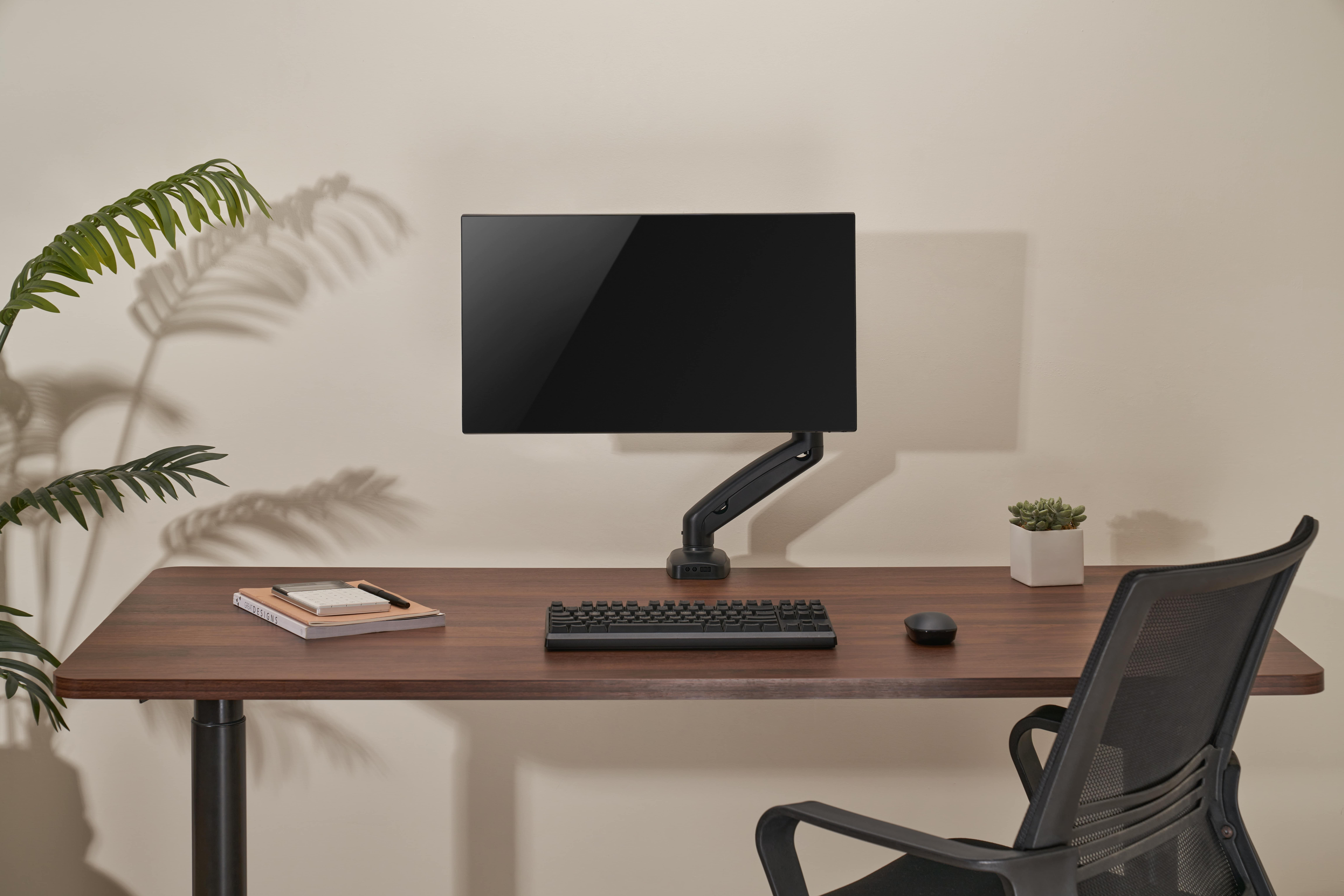 Schreibtisch mit Monitor, Tastatur, Maus, Notizbuch und Stuhl.