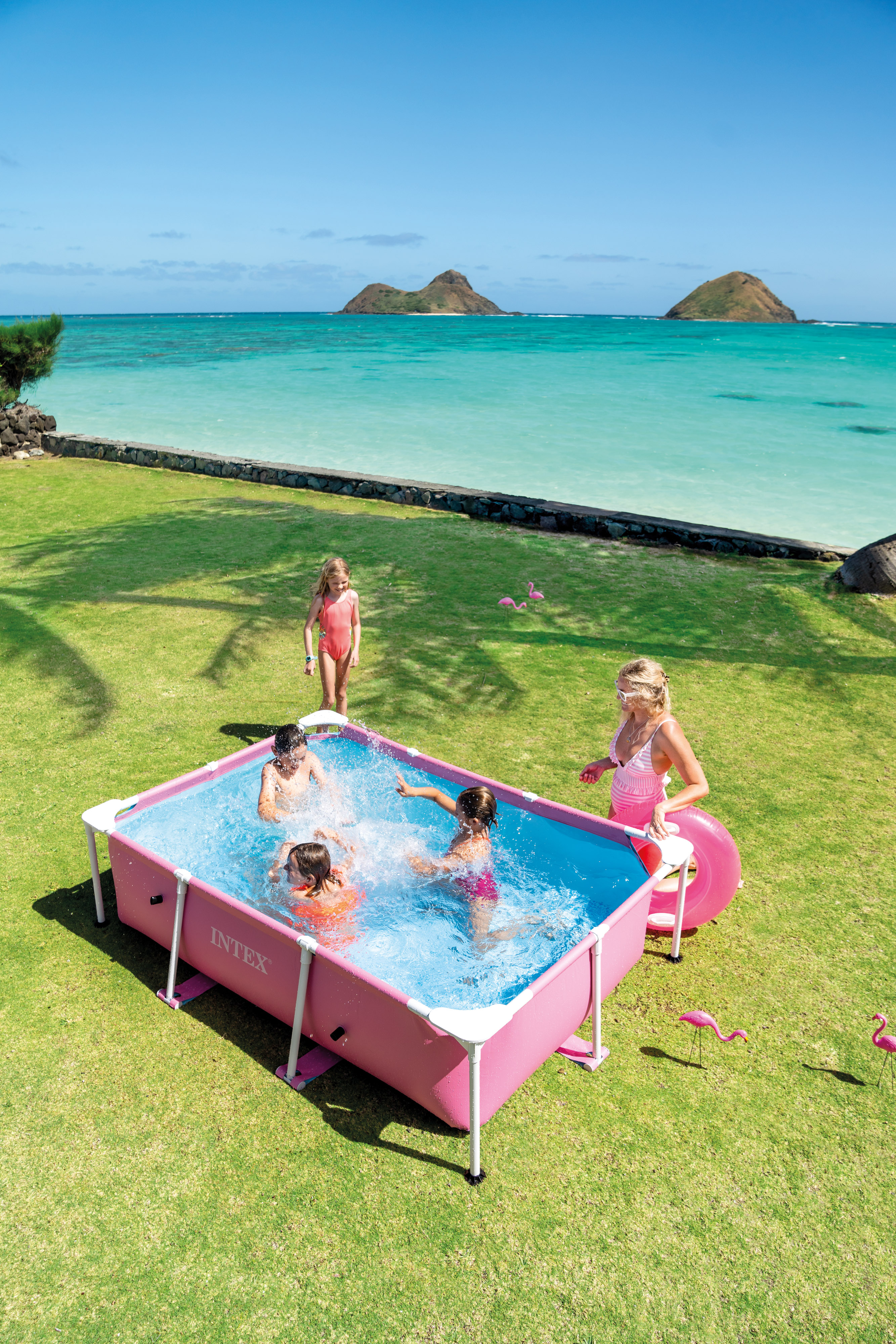Kinder planschen in einem rosafarbenen Pool am Strand mit Blick auf die Inseln.