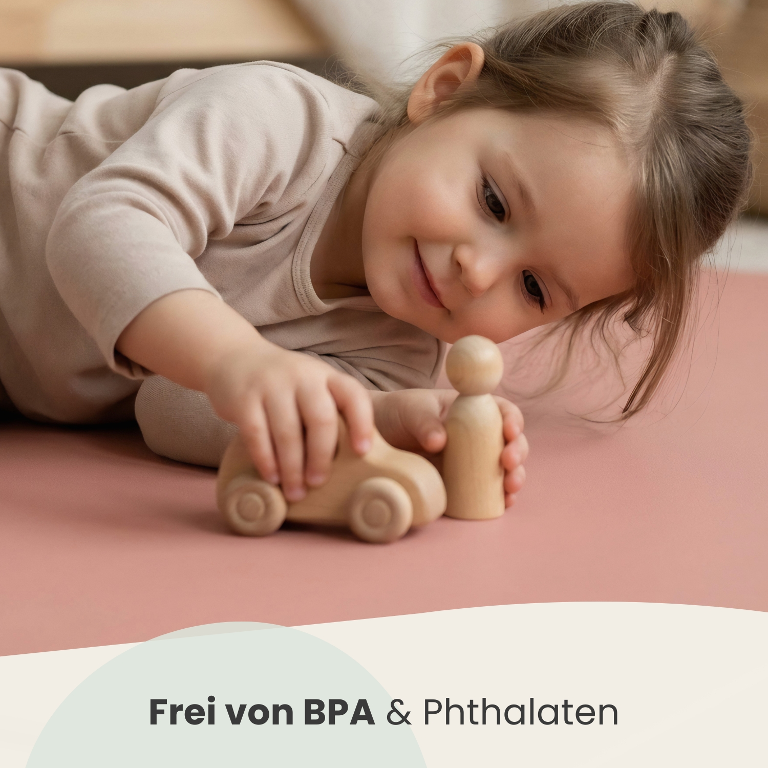 Ein kleines Mädchen spielt mit einem Holzauto und einer Holzfigur auf einer rosafarbenen Matte.