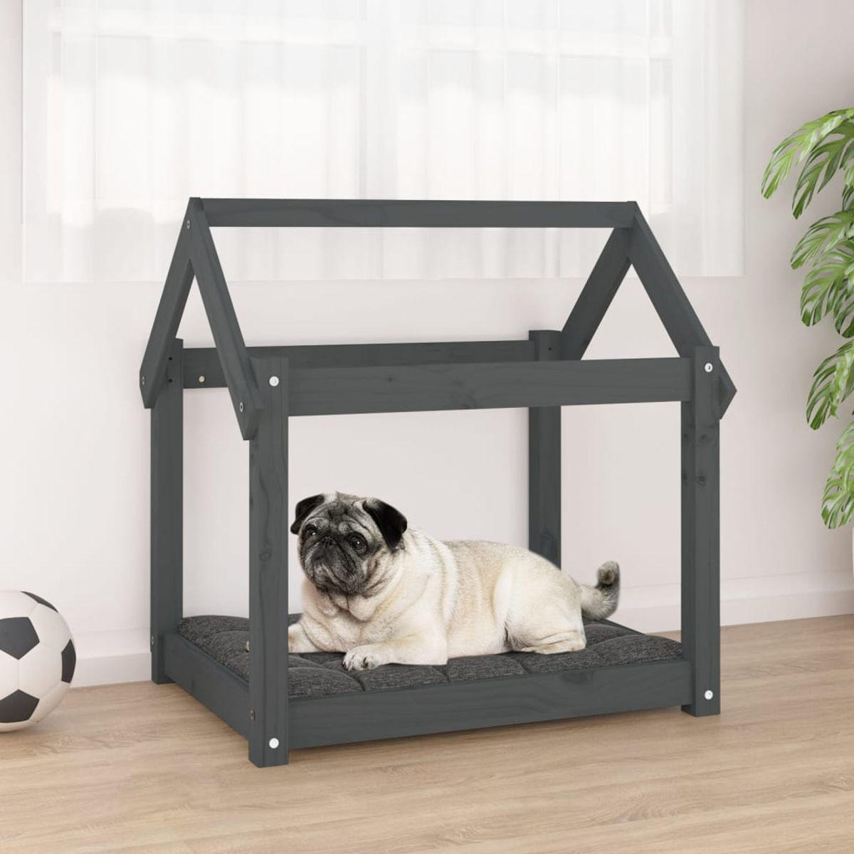 Ein Mops liegt auf einem Kissen in einem grauen Holzhundhaus. Links ein Ball.