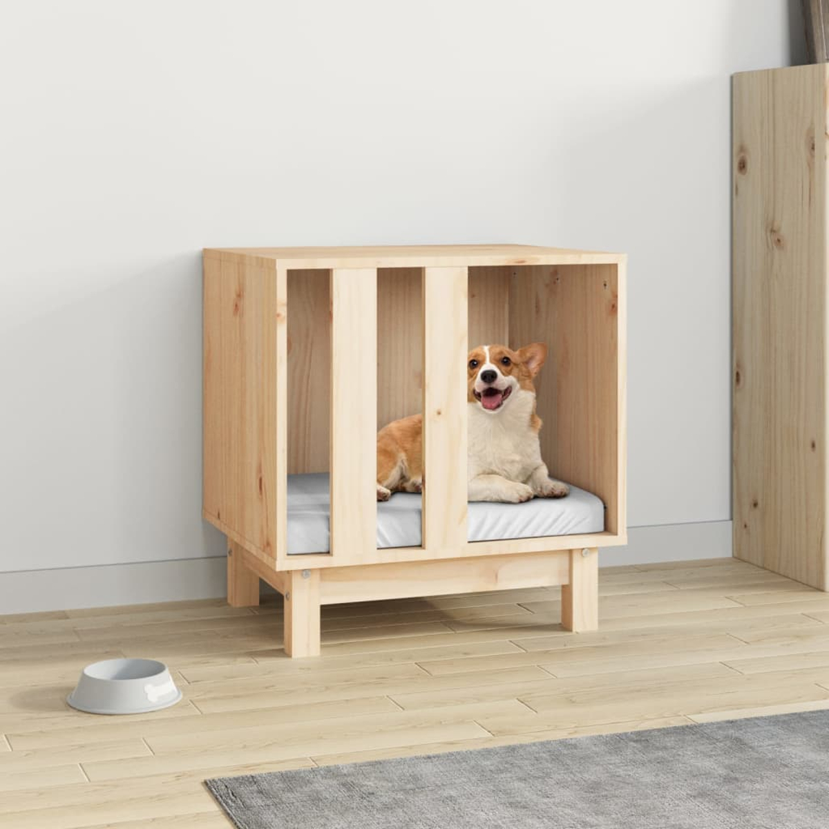 Ein Corgi liegt in einer Holzhütte mit einem grauen Napf und einer Decke daneben.
