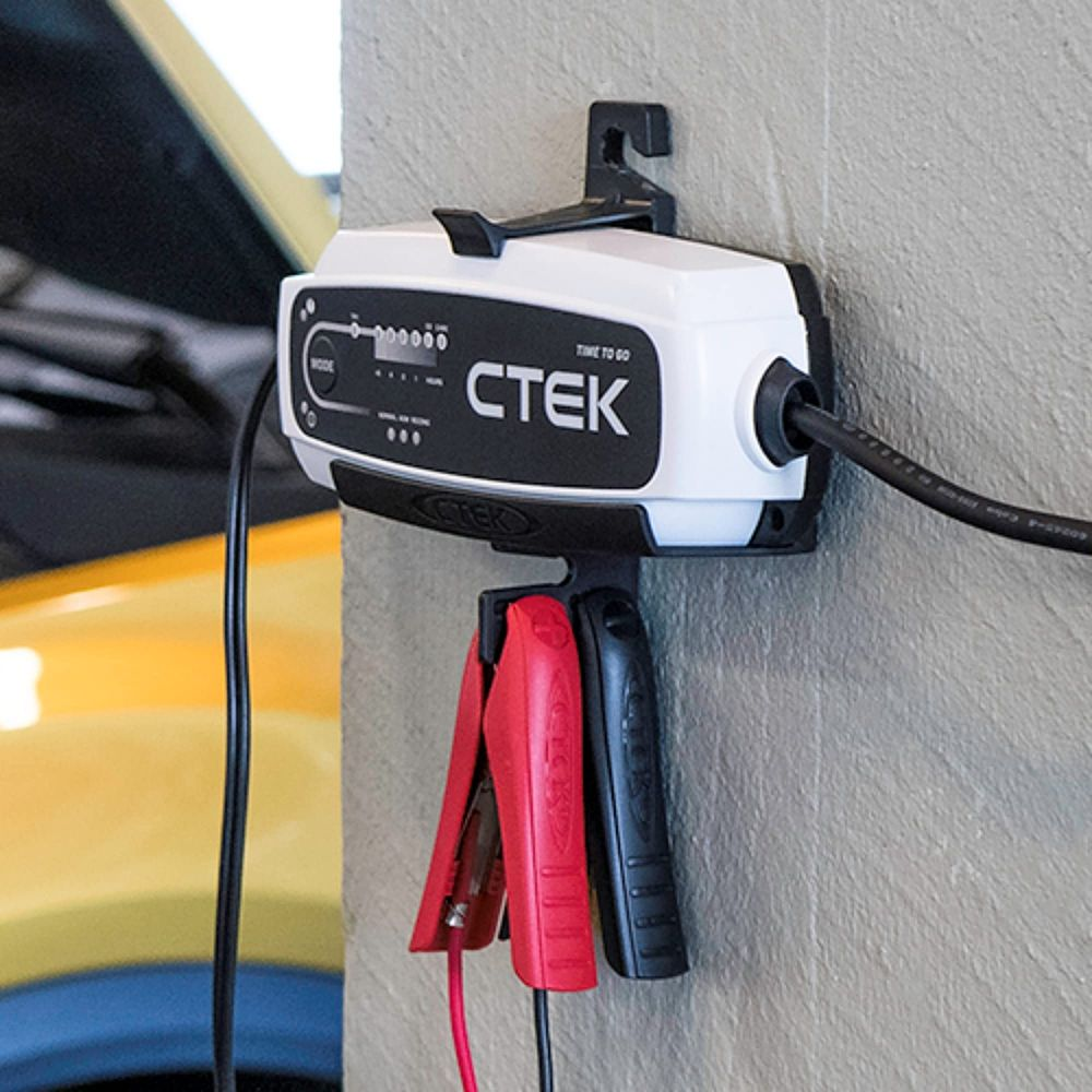 Ein CTEK Batterieladegerät mit roten und schwarzen Klemmen hängt an einer Wand.