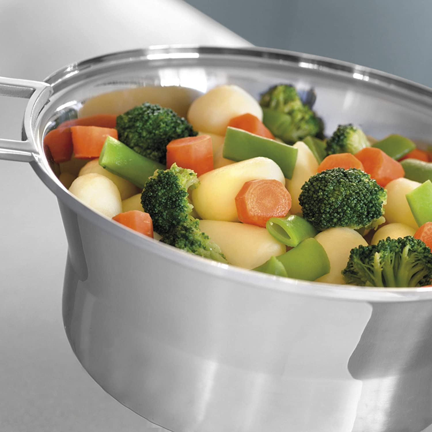 Stalowy garnek wypełniony gotowanymi warzywami, w tym ziemniakami, marchewką i brokułami.