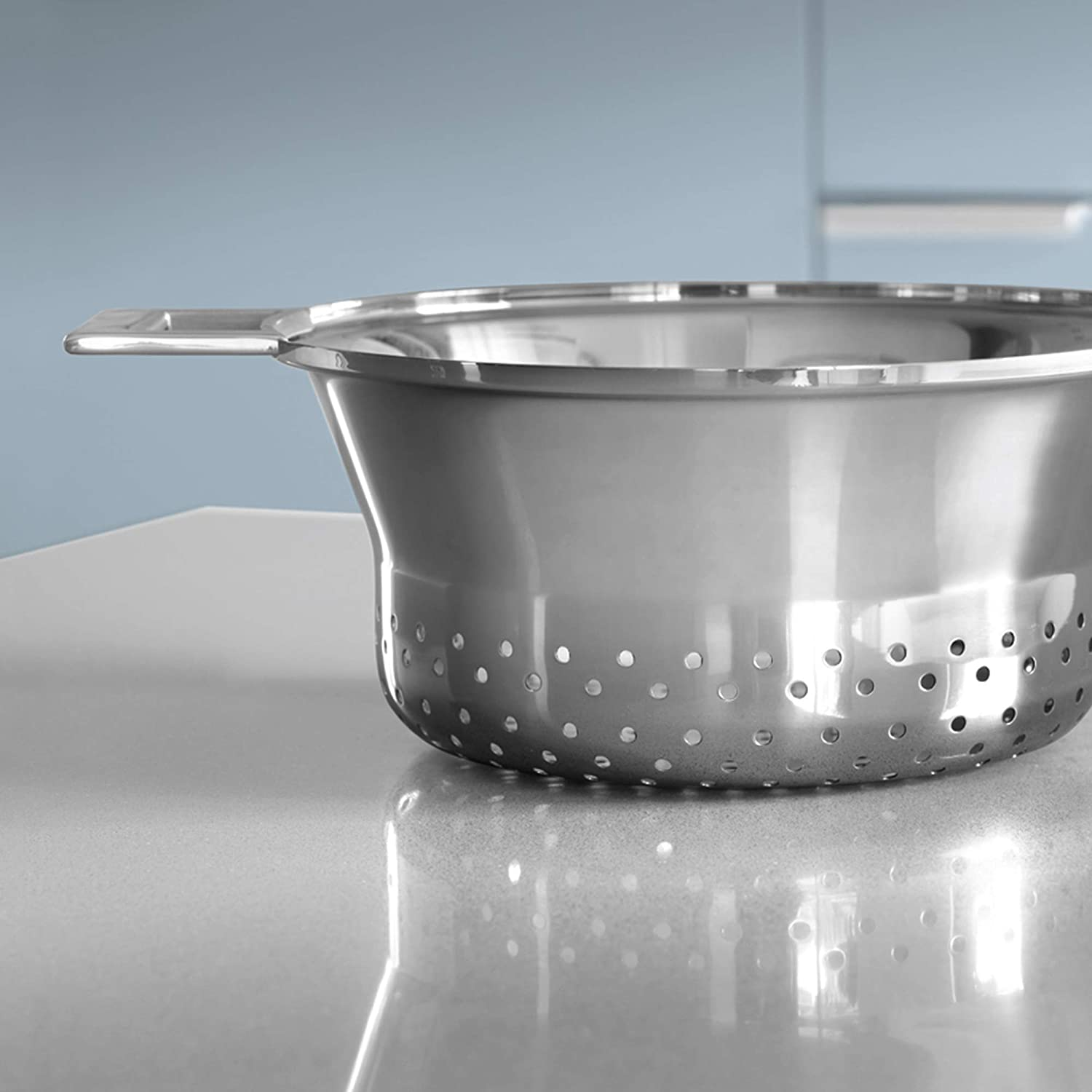 Srebrne sitko z małymi dziurkami stoi na szarej powierzchni.