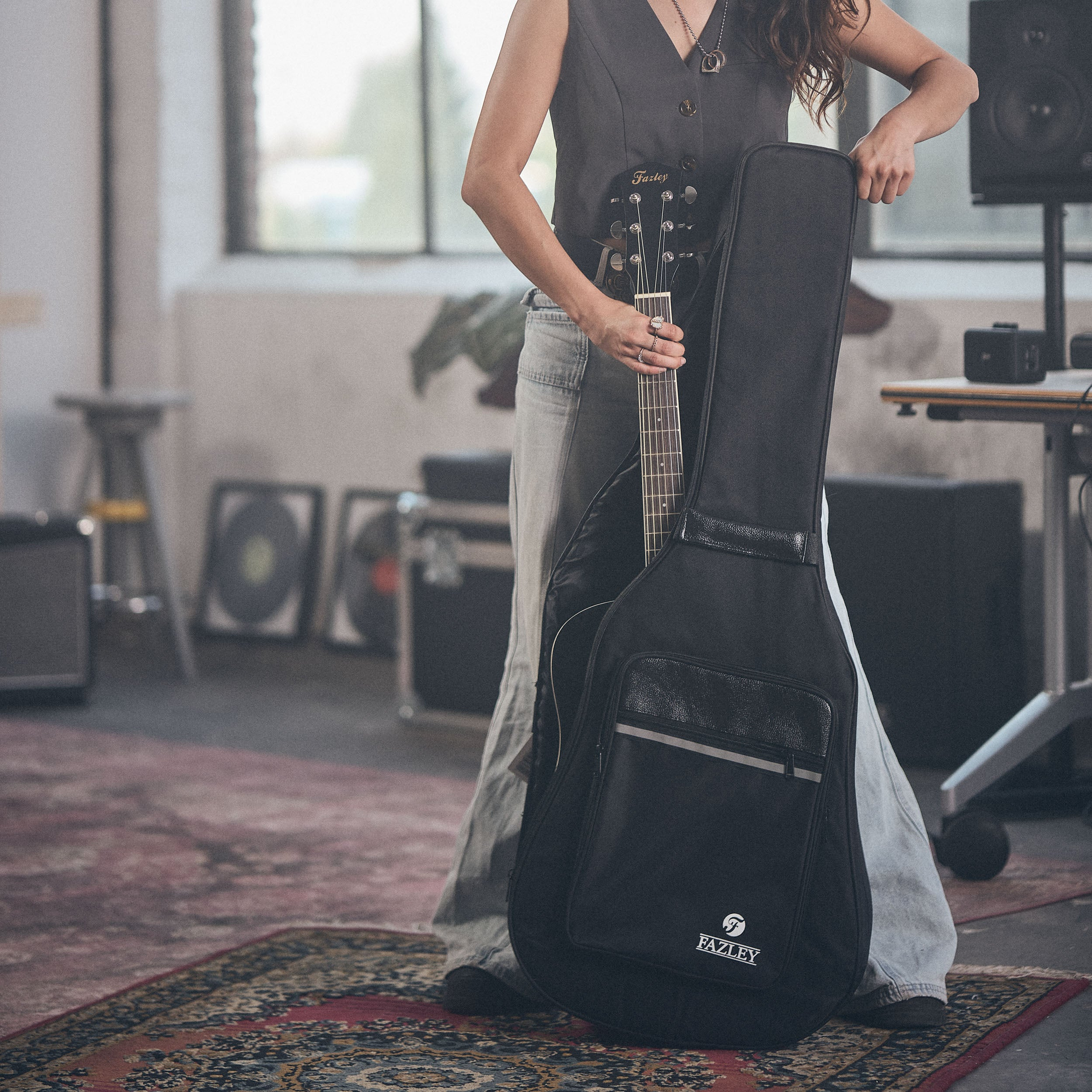 A person holds a guitar in a black case in a studio setting.
