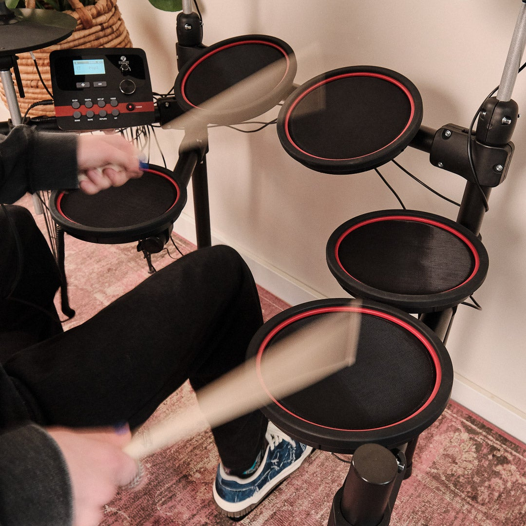 Persoon bespeelt elektronische drumstel met stokken, close-up van pads en console.