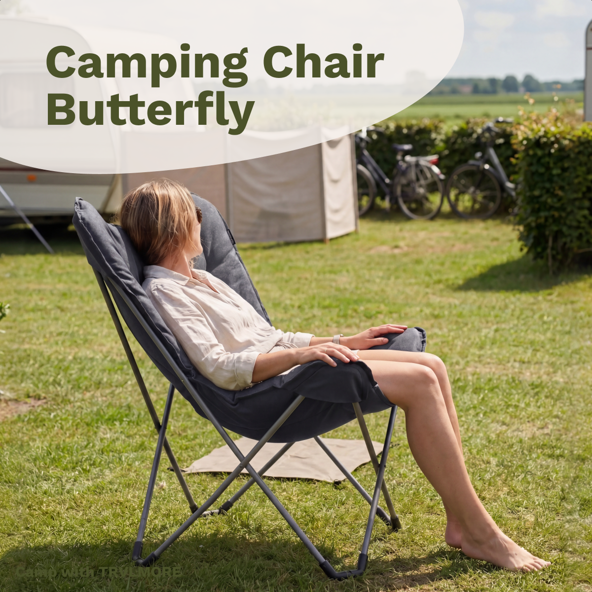 Woman sits in a dark camping chair outdoors, with caravan and bicycles in the background.