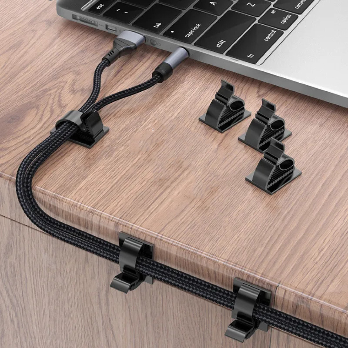 Schwarze Kabel werden von Clips an einem Holztisch gehalten, die in einen Laptop gesteckt sind.