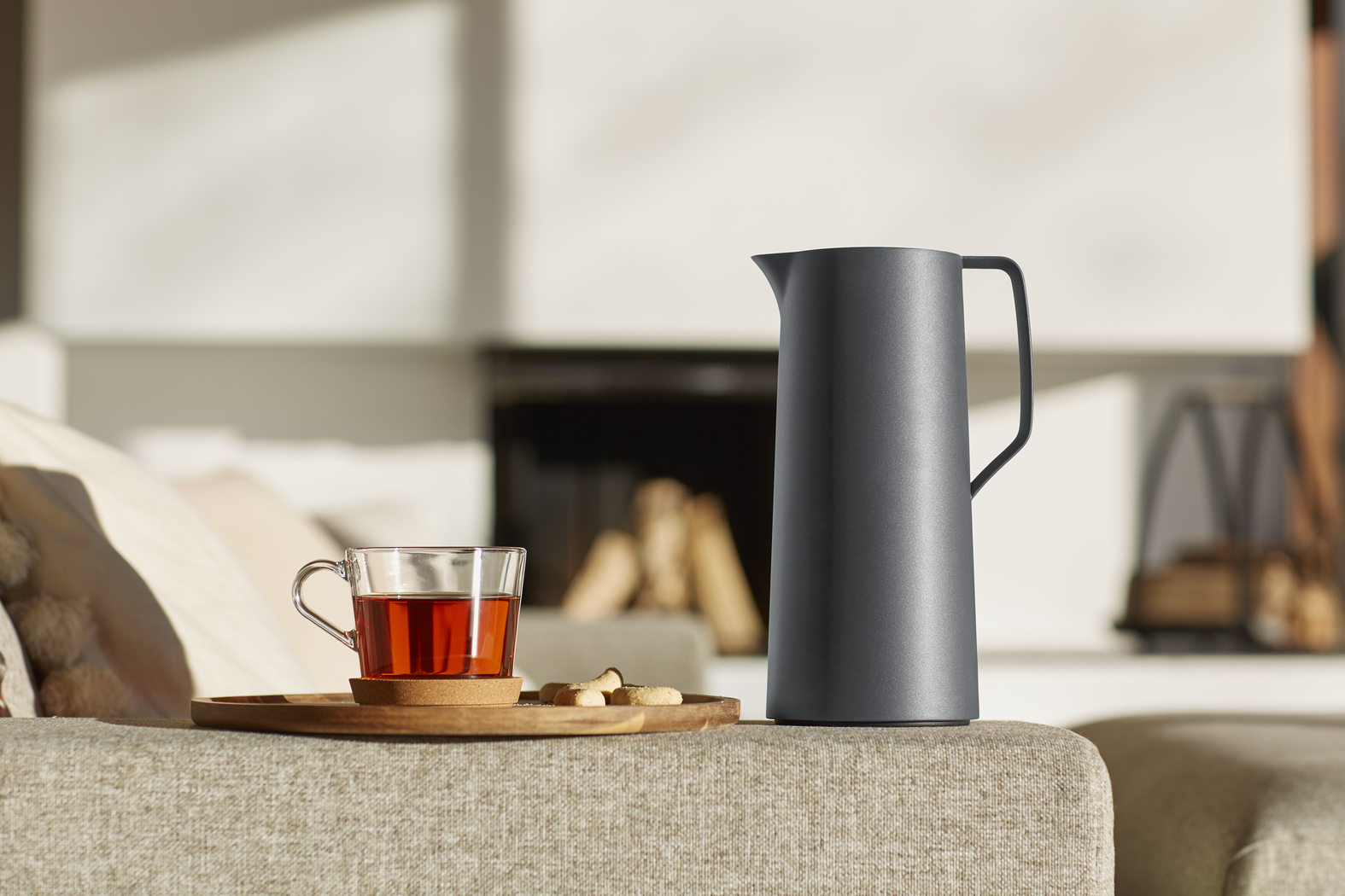 Una jarra térmica gris y un vaso de té con galletas sobre una mesa.