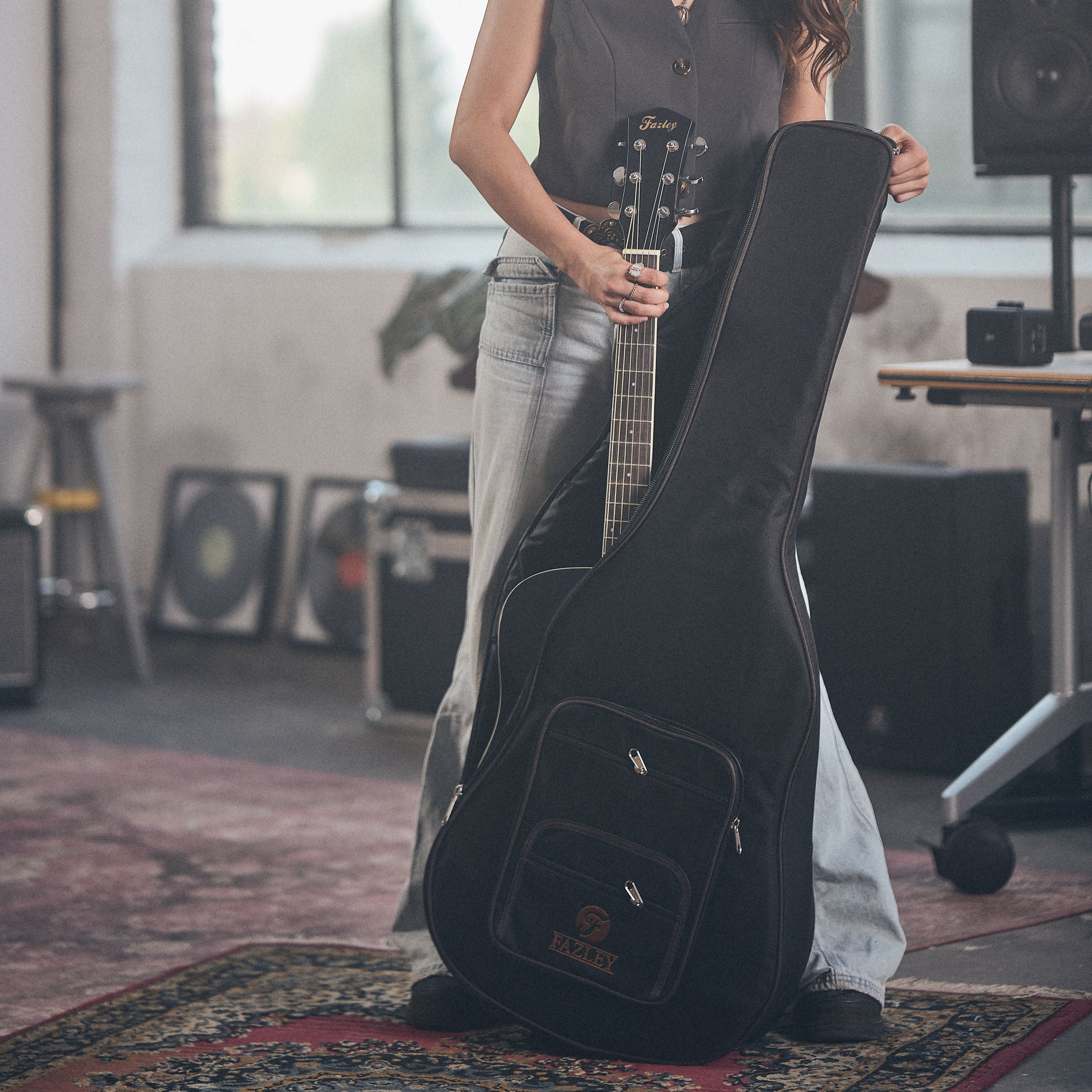 Een persoon houdt een gitaar in een zwarte koffer in een studio.