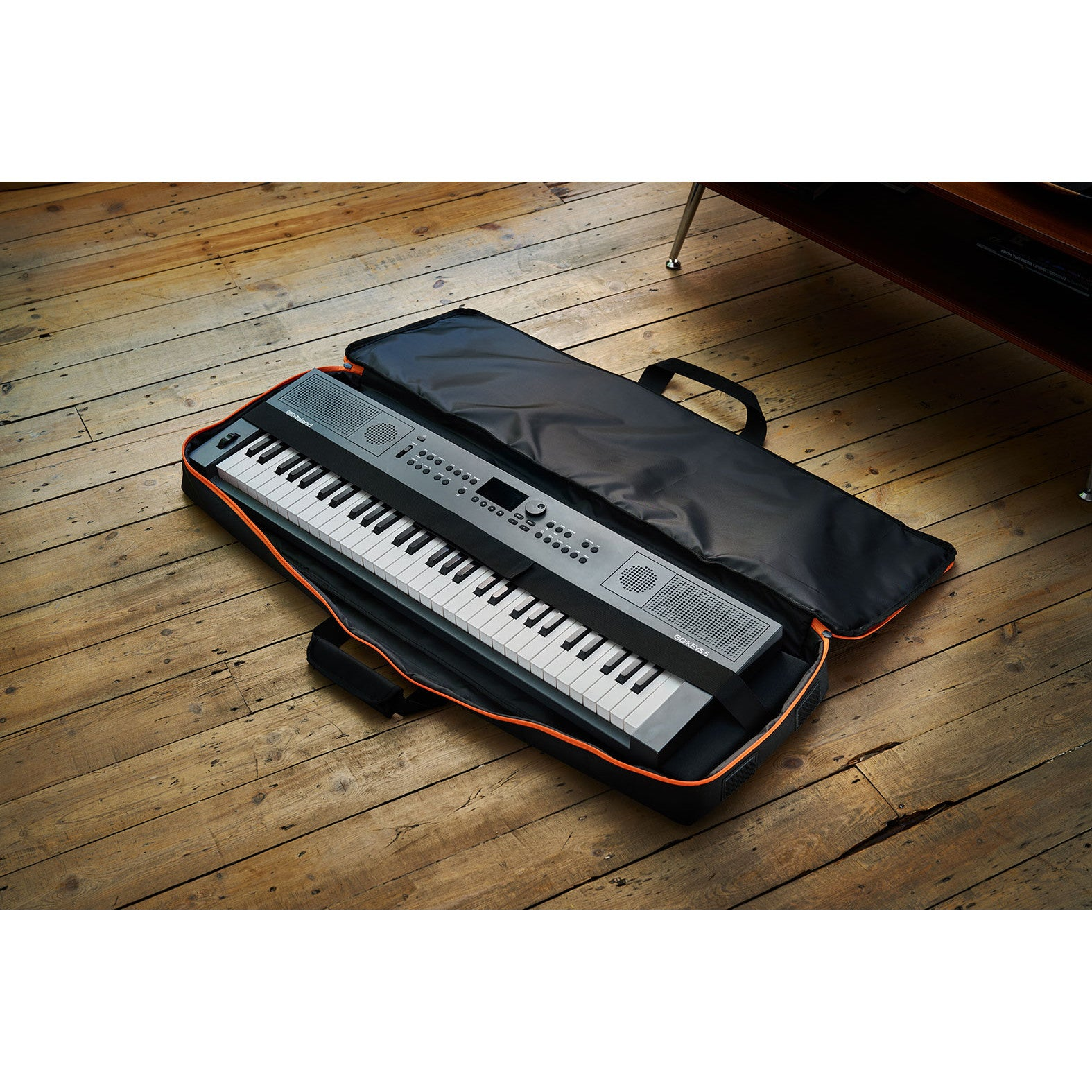 Een grijs keyboard met zwart-witte toetsen ligt in een zwarte hoes op houten vloerplanken.