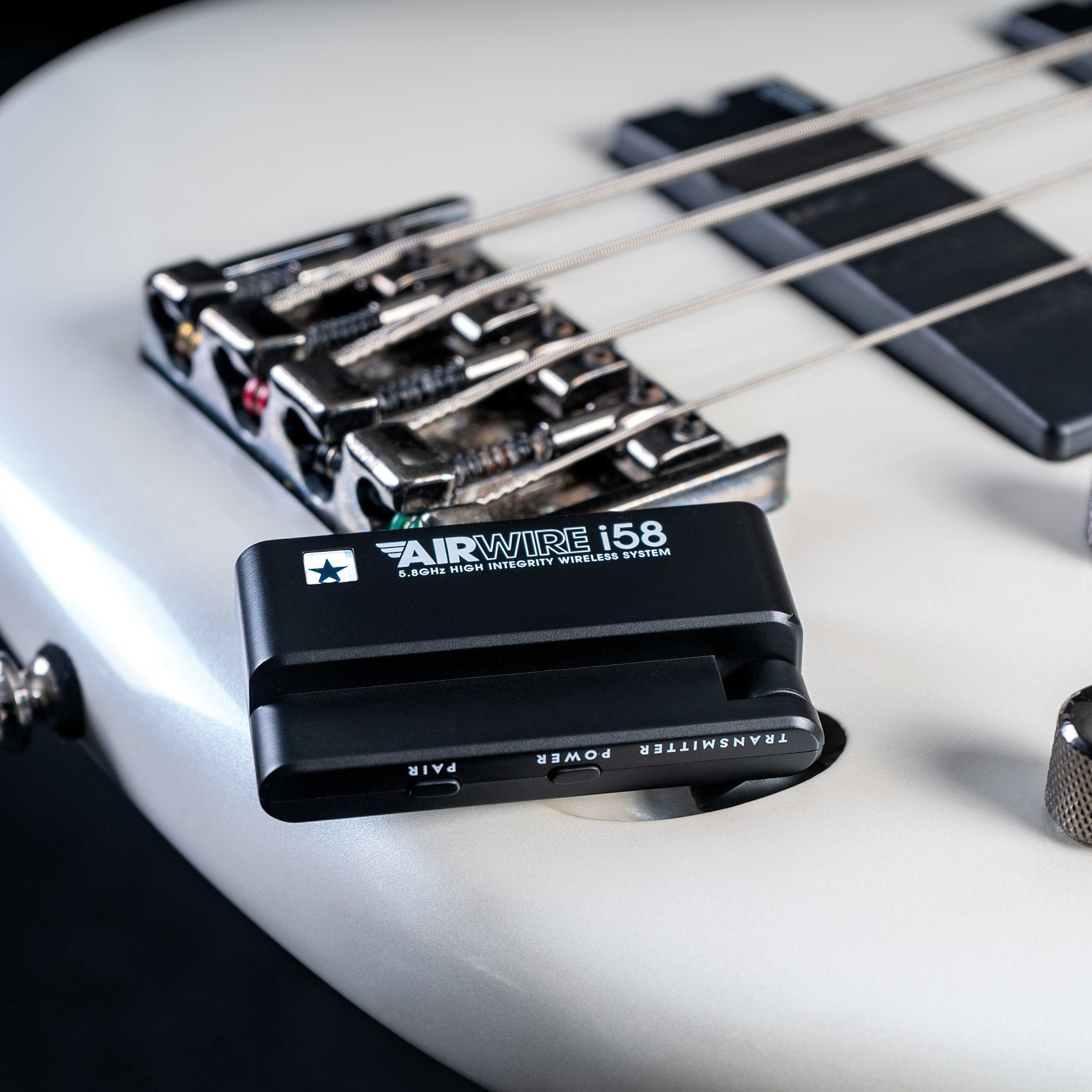 A black wireless transmitter sits on a white bass guitar bridge.