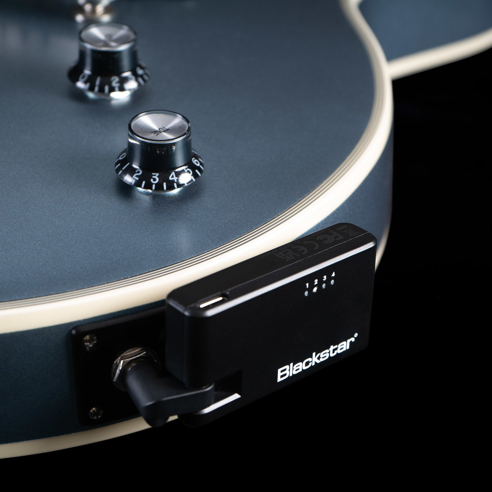 A black Blackstar guitar transmitter is plugged into the jack of a blue guitar body.