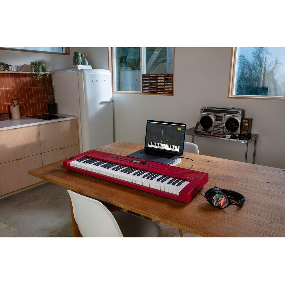 Een rood keyboard staat op een houten tafel naast een laptop met bladmuziek.