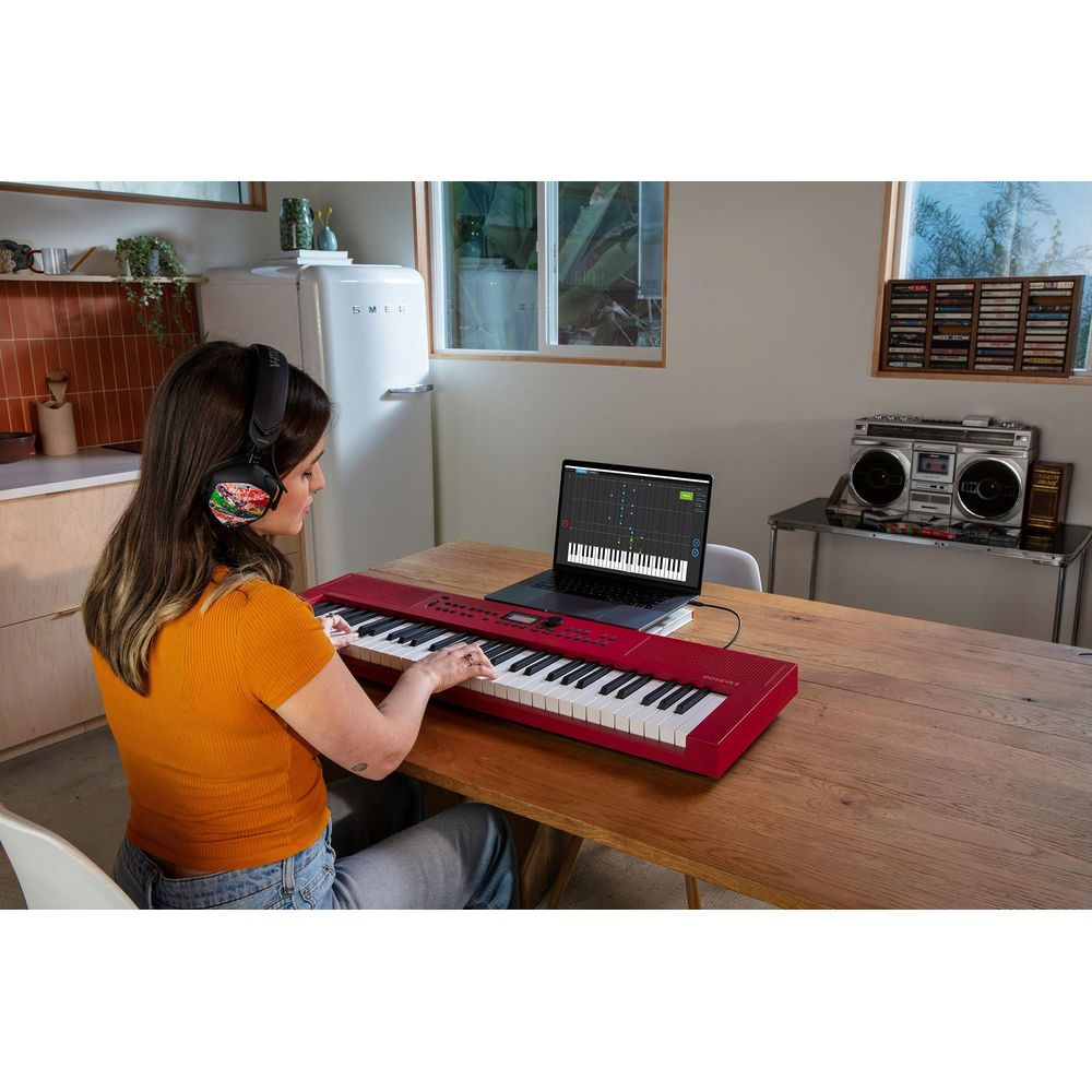 Vrouw speelt op een rood keyboard naast een laptop met bladmuziek.