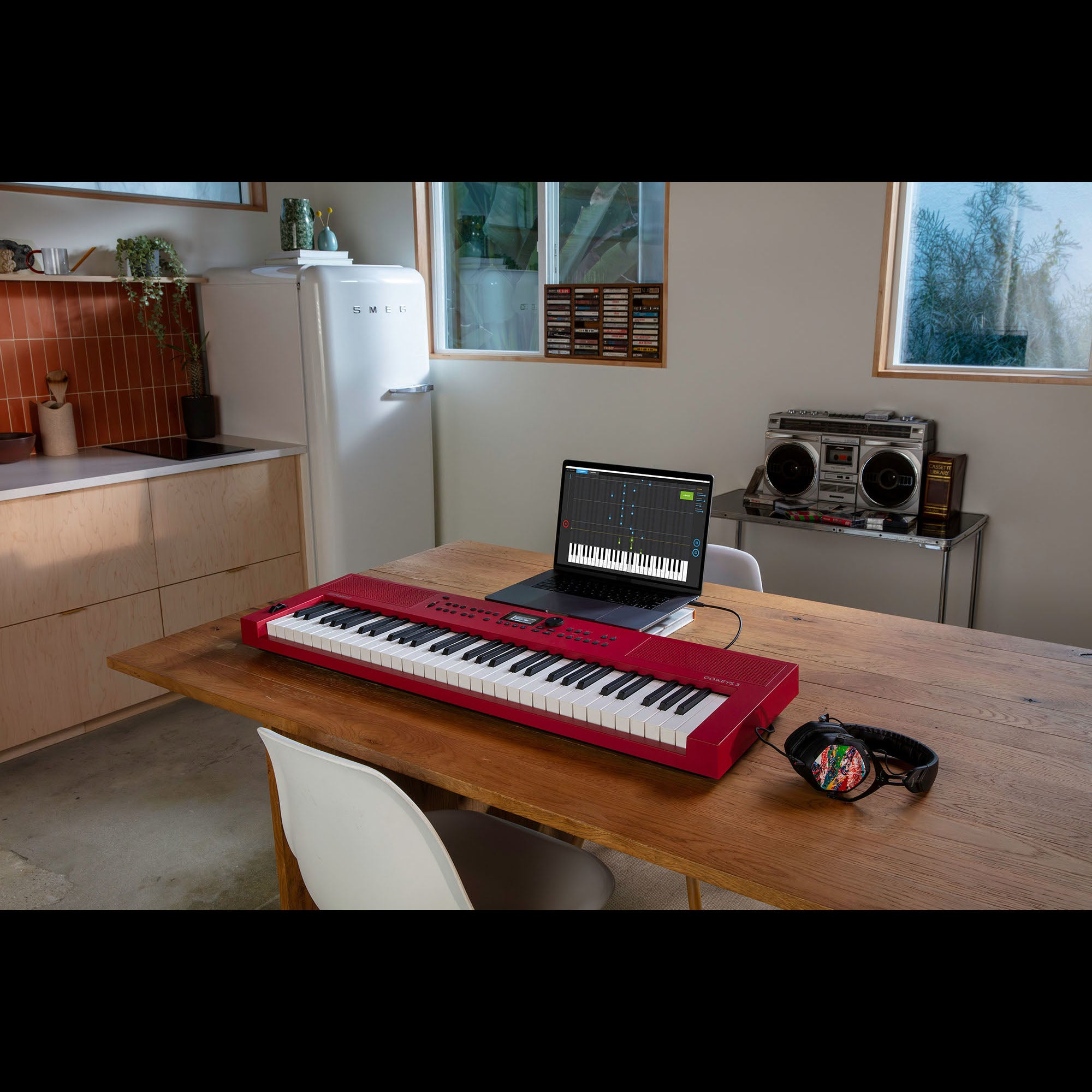 Een rood keyboard staat op een houten tafel voor een laptop met muzieksoftware erop.