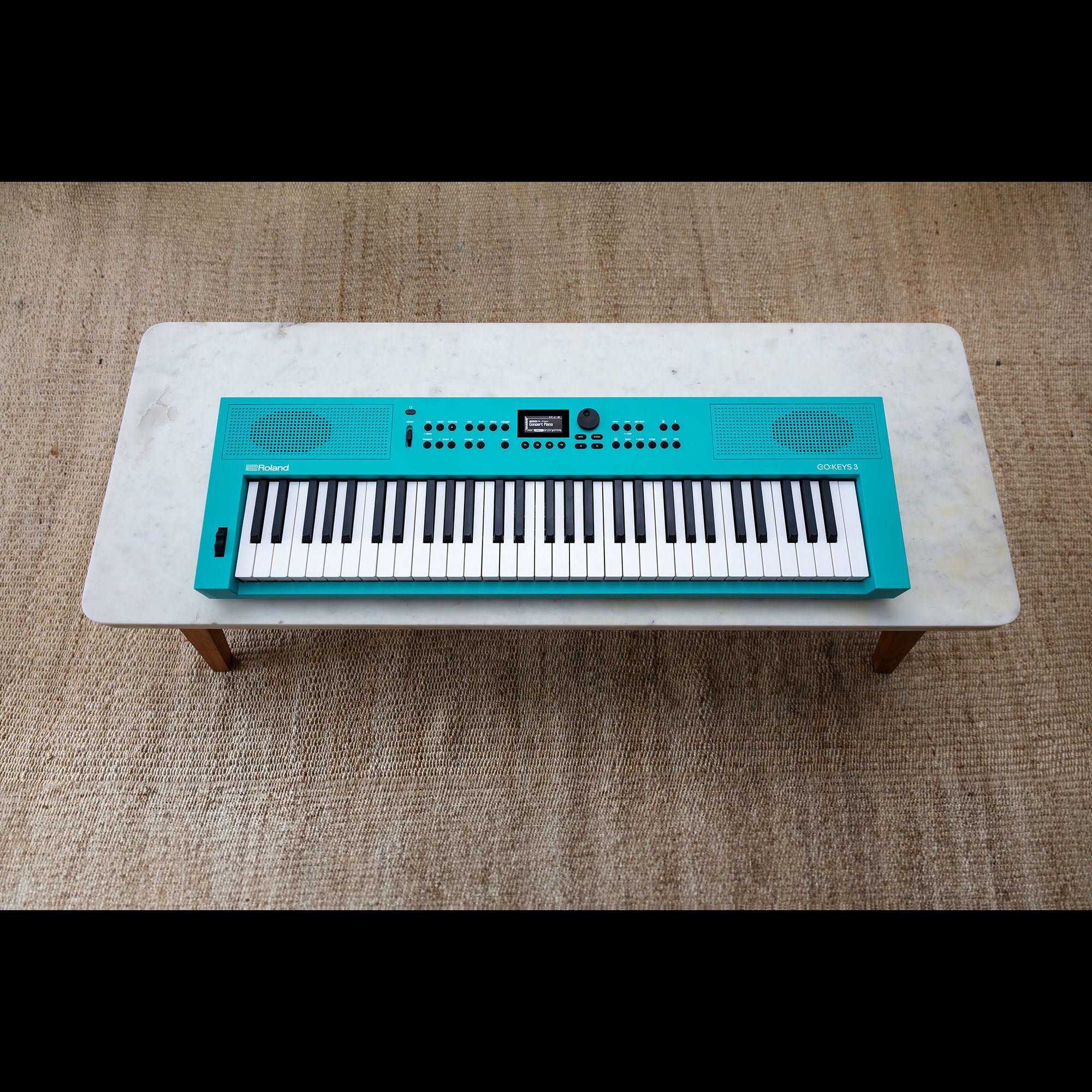 Een turquoise Roland GO:KEYS 3 synthesizer met zwarte en witte toetsen op een marmeren tafel.