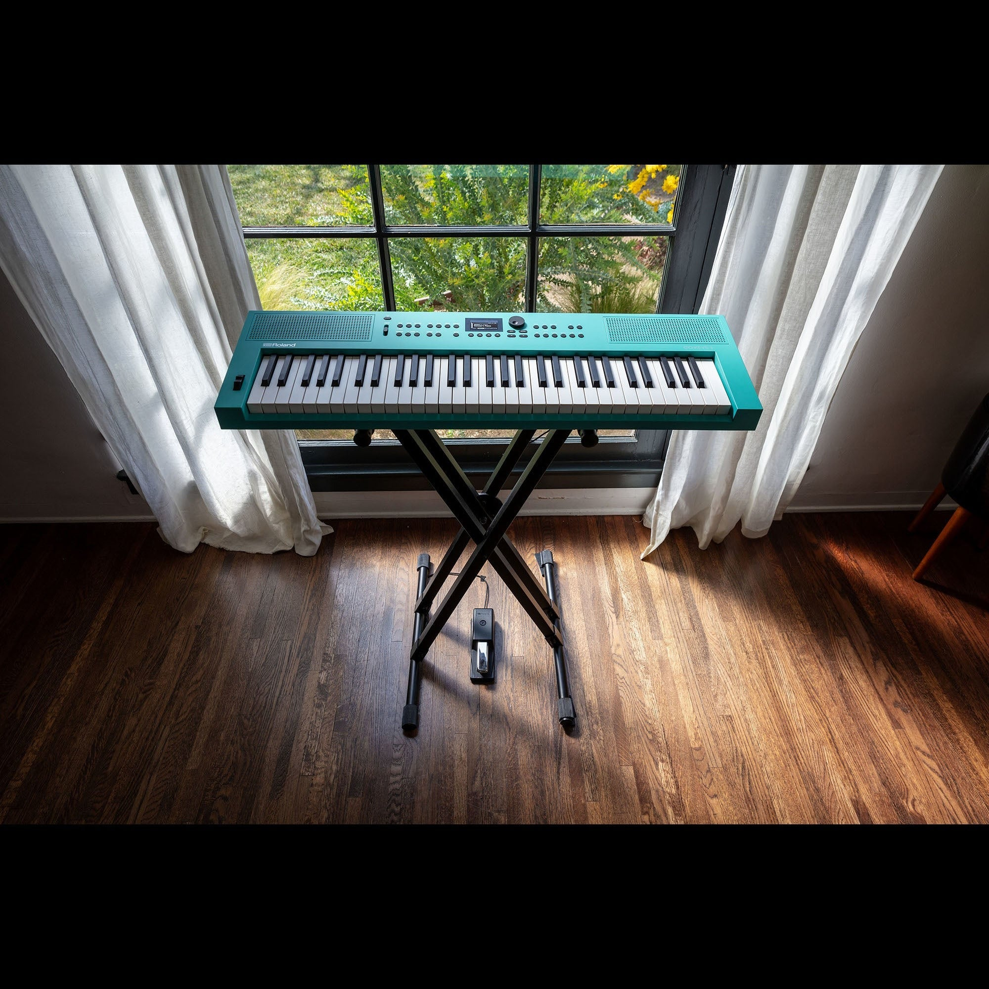 Een turquoise keyboard staat op een zwarte standaard voor een raam met gordijnen.
