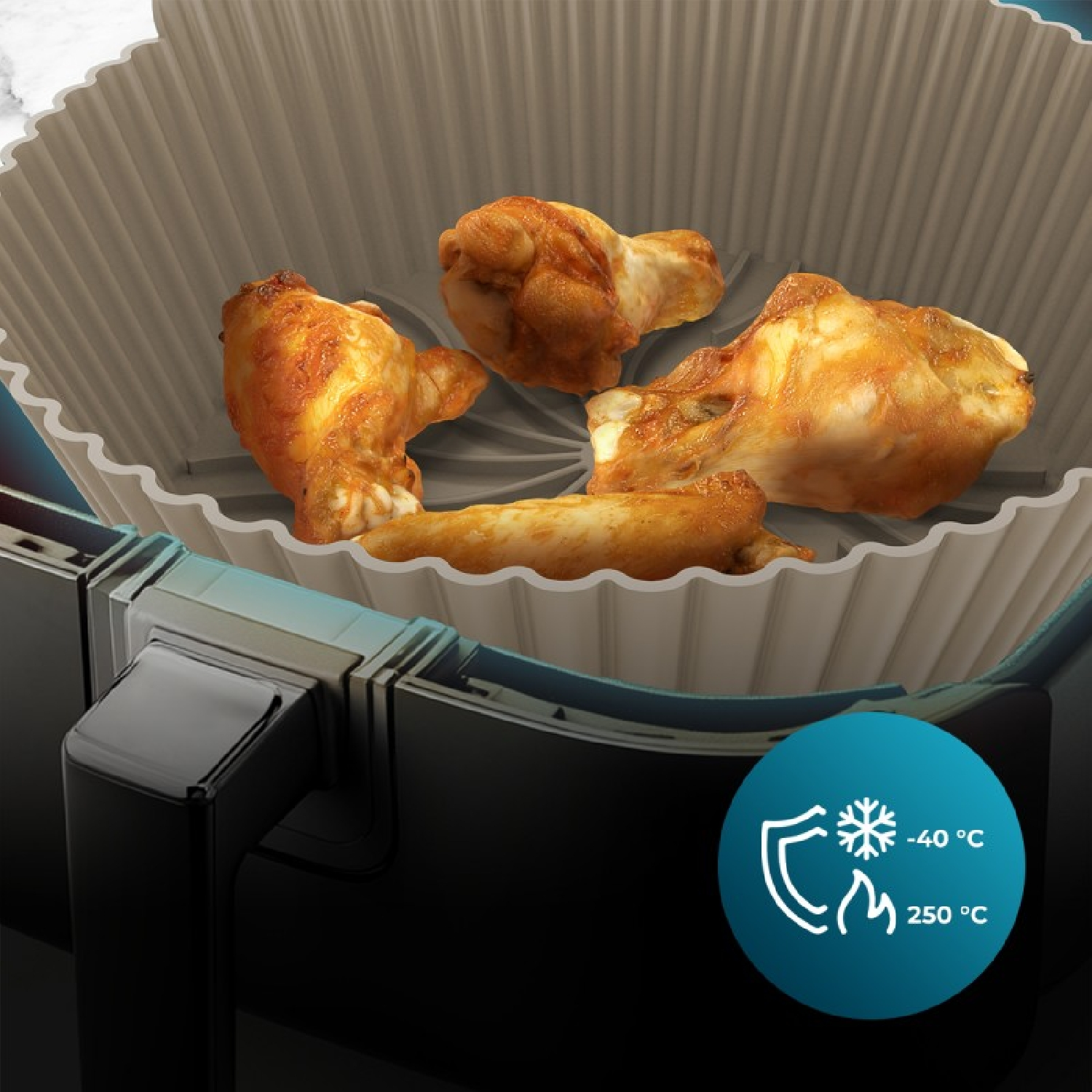 Alitas de pollo doradas en un revestimiento de silicona acanalado dentro de una freidora.