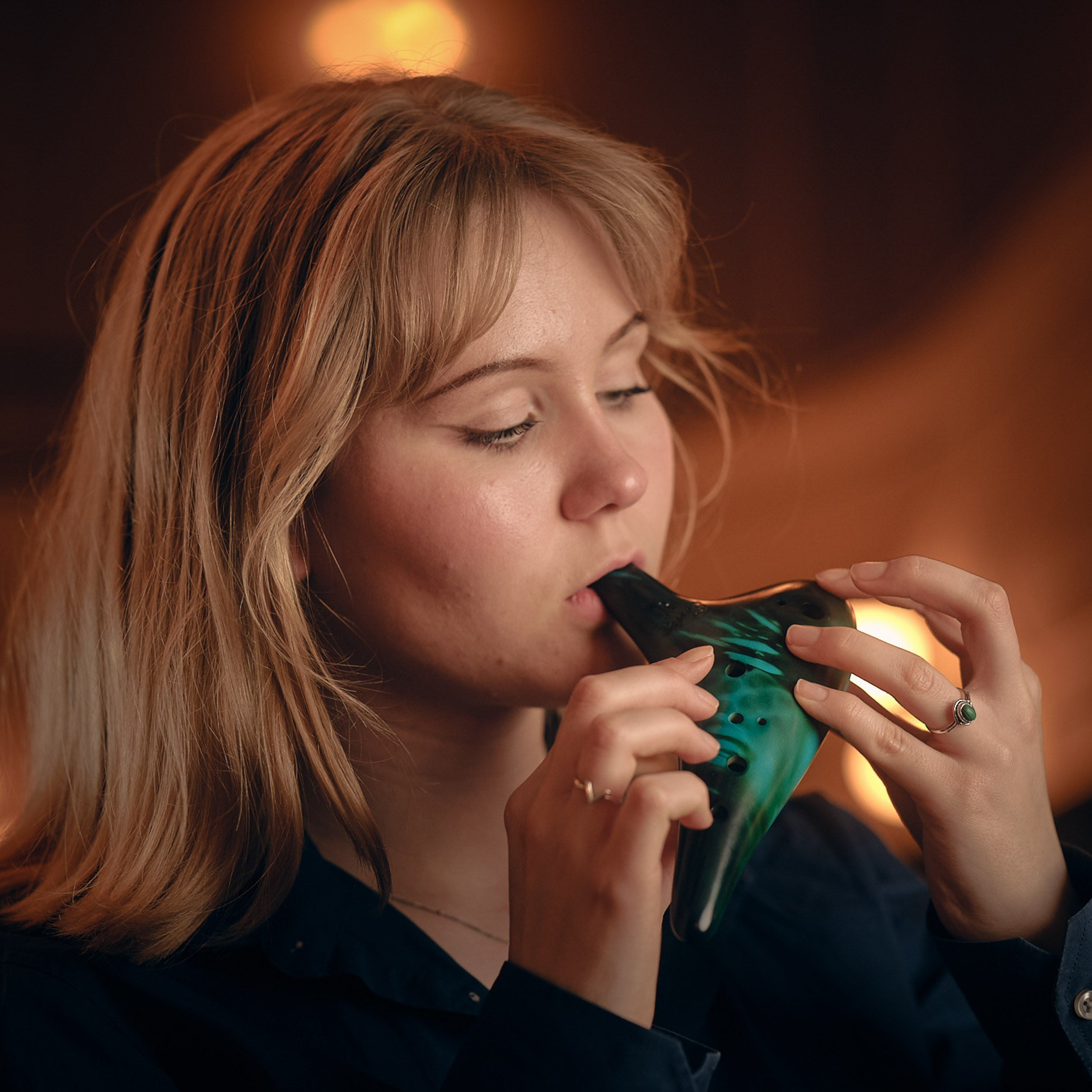 A young woman with blonde hair plays a green ocarina.