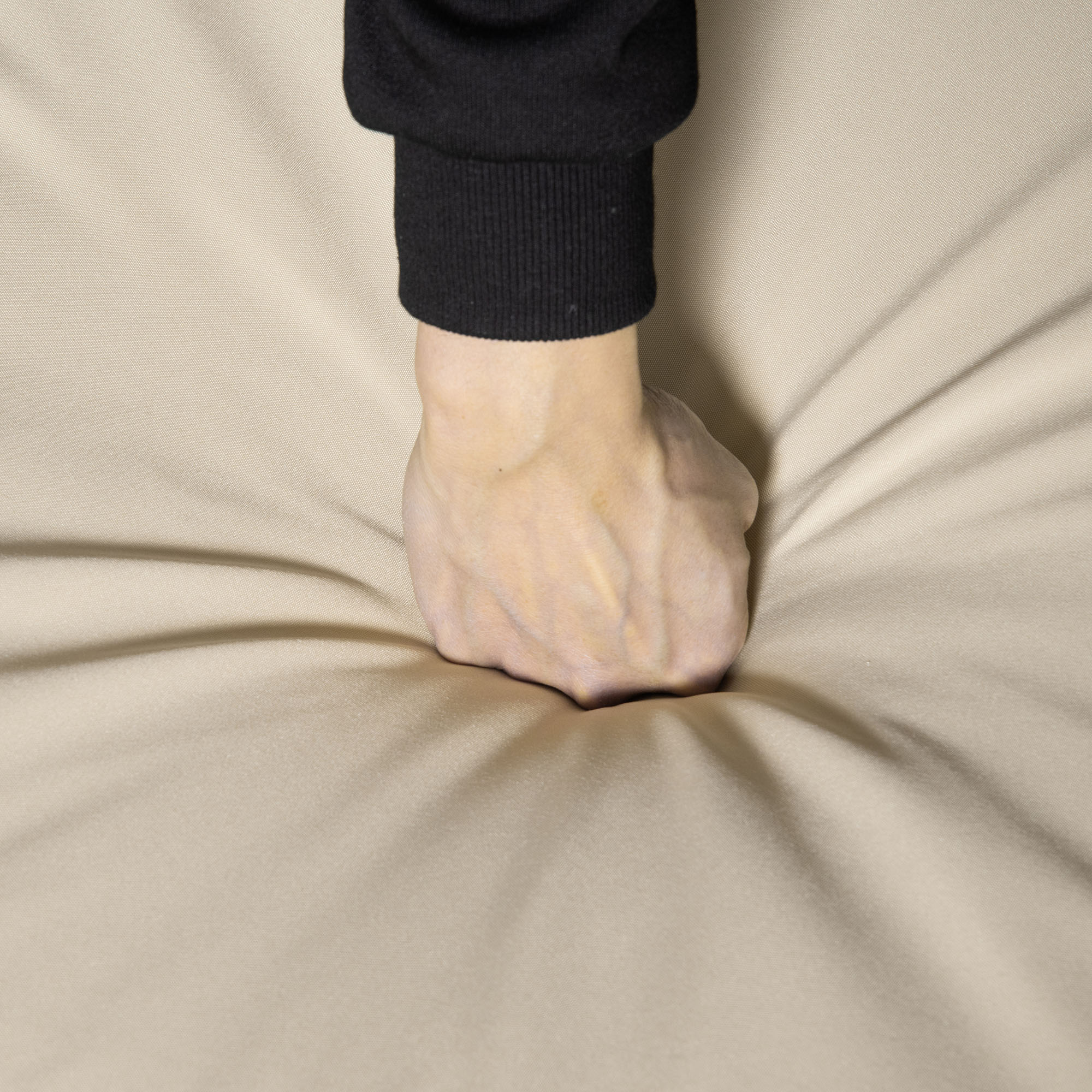 Un puño presiona tela beige claro. La tela está arrugada.