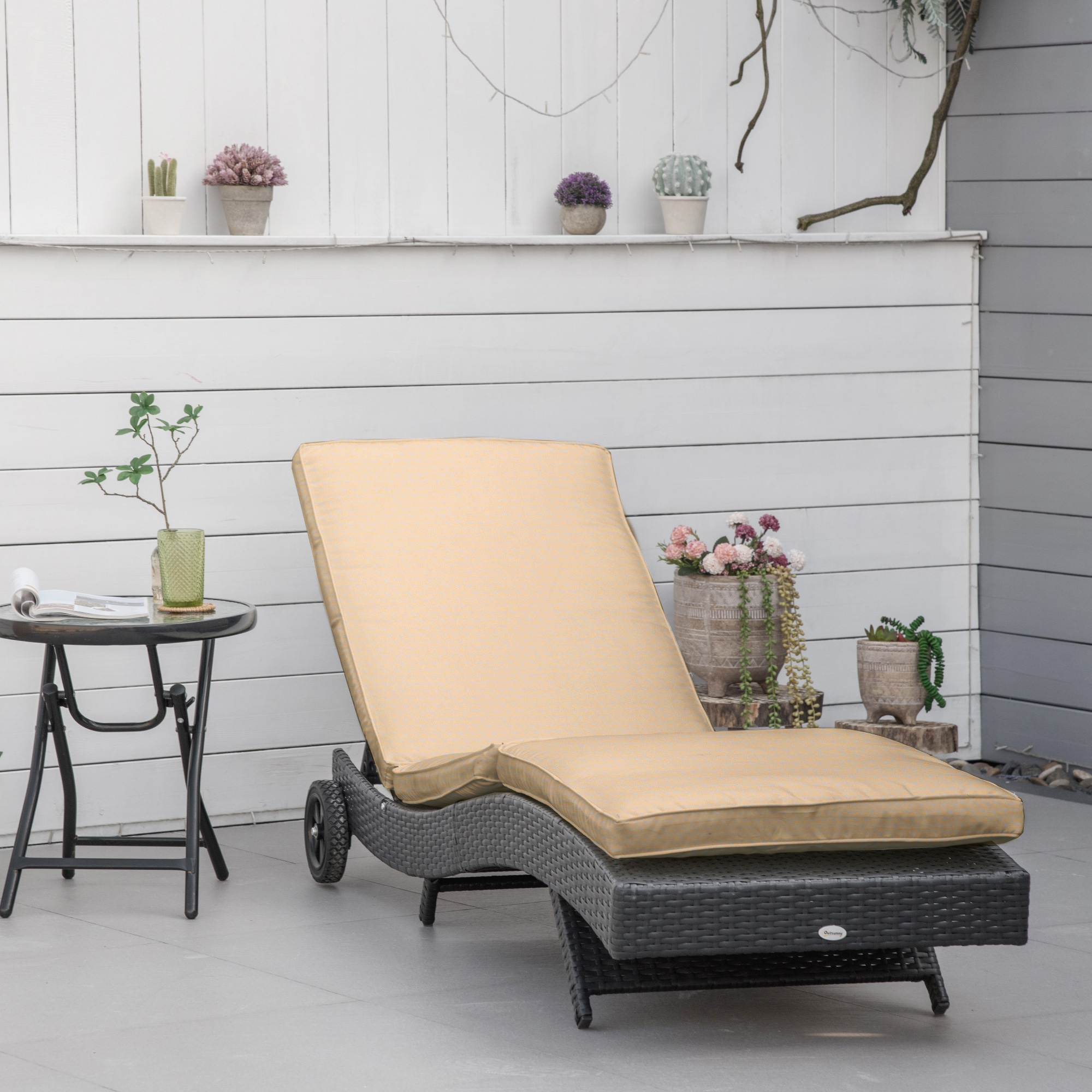 Un lettino prendisole in vimini scuro con cuscino beige si trova su un patio vicino a un tavolino.
