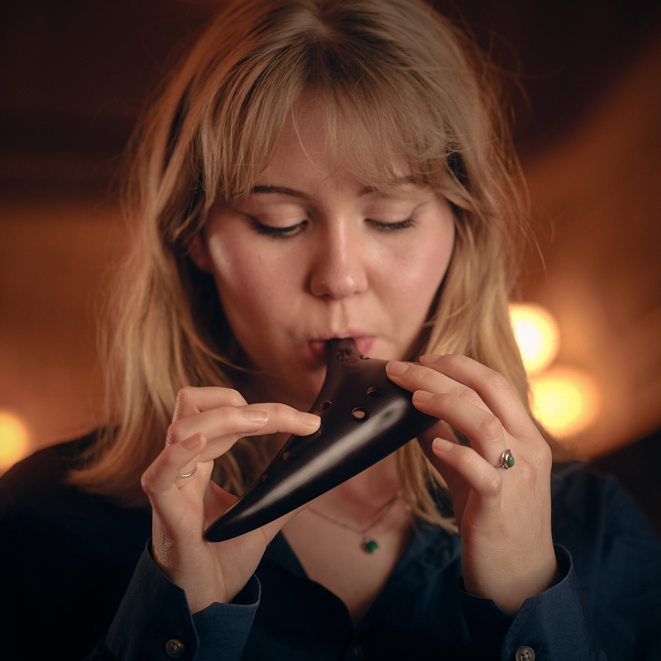 A woman with blonde hair plays a dark ocarina.