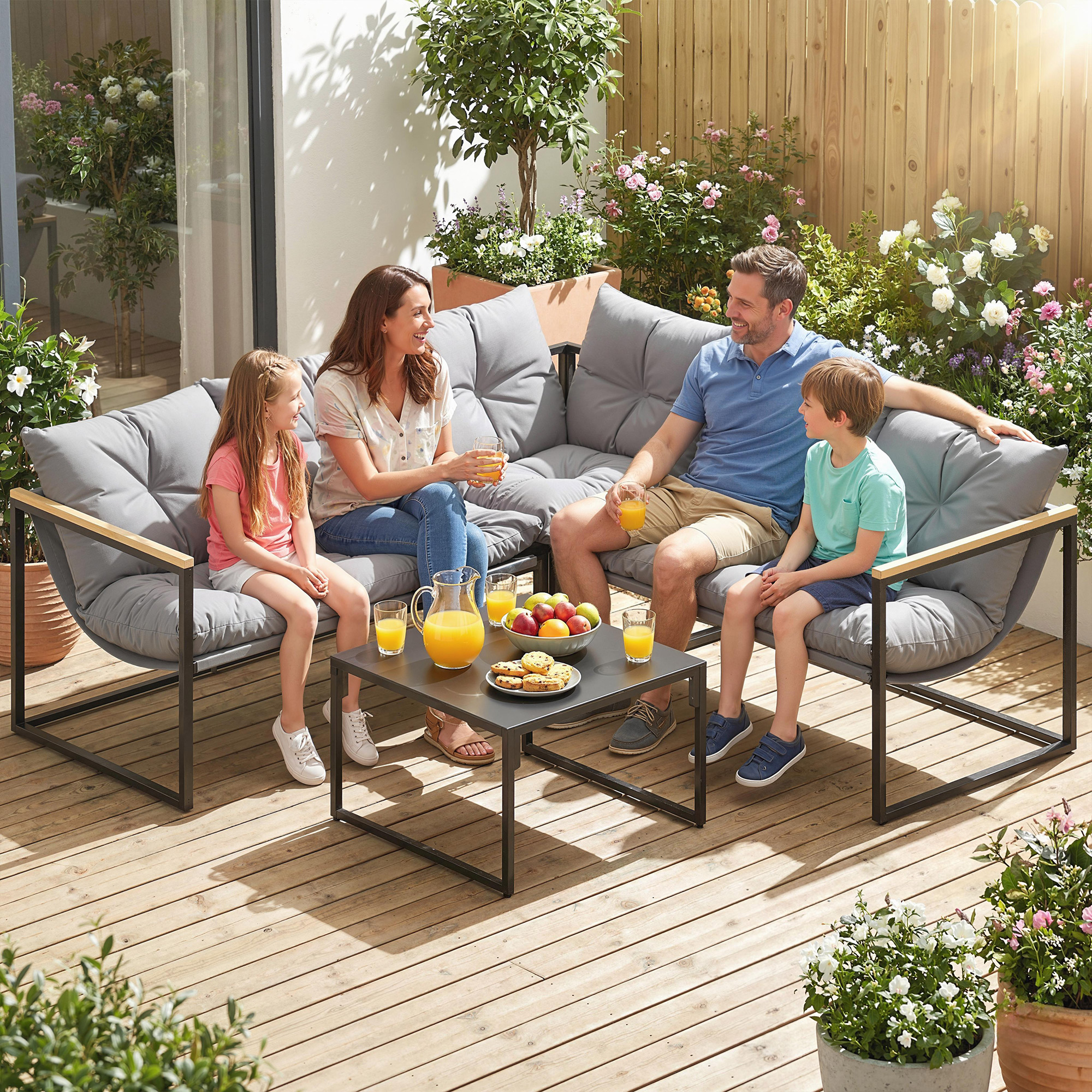 Familia disfruta de bebidas y aperitivos en un sofá de jardín entre flores.
