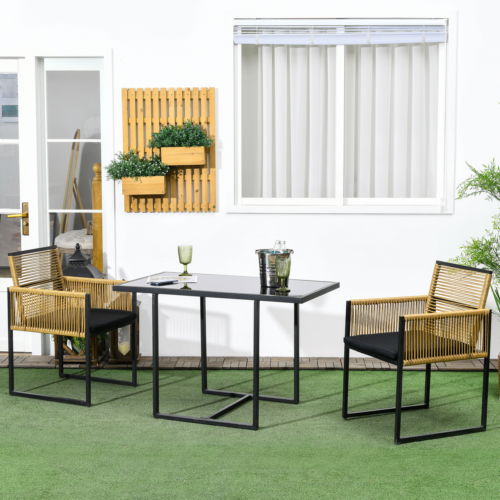 Una mesa y dos sillas sobre césped artificial frente a una pared blanca con ventanas.