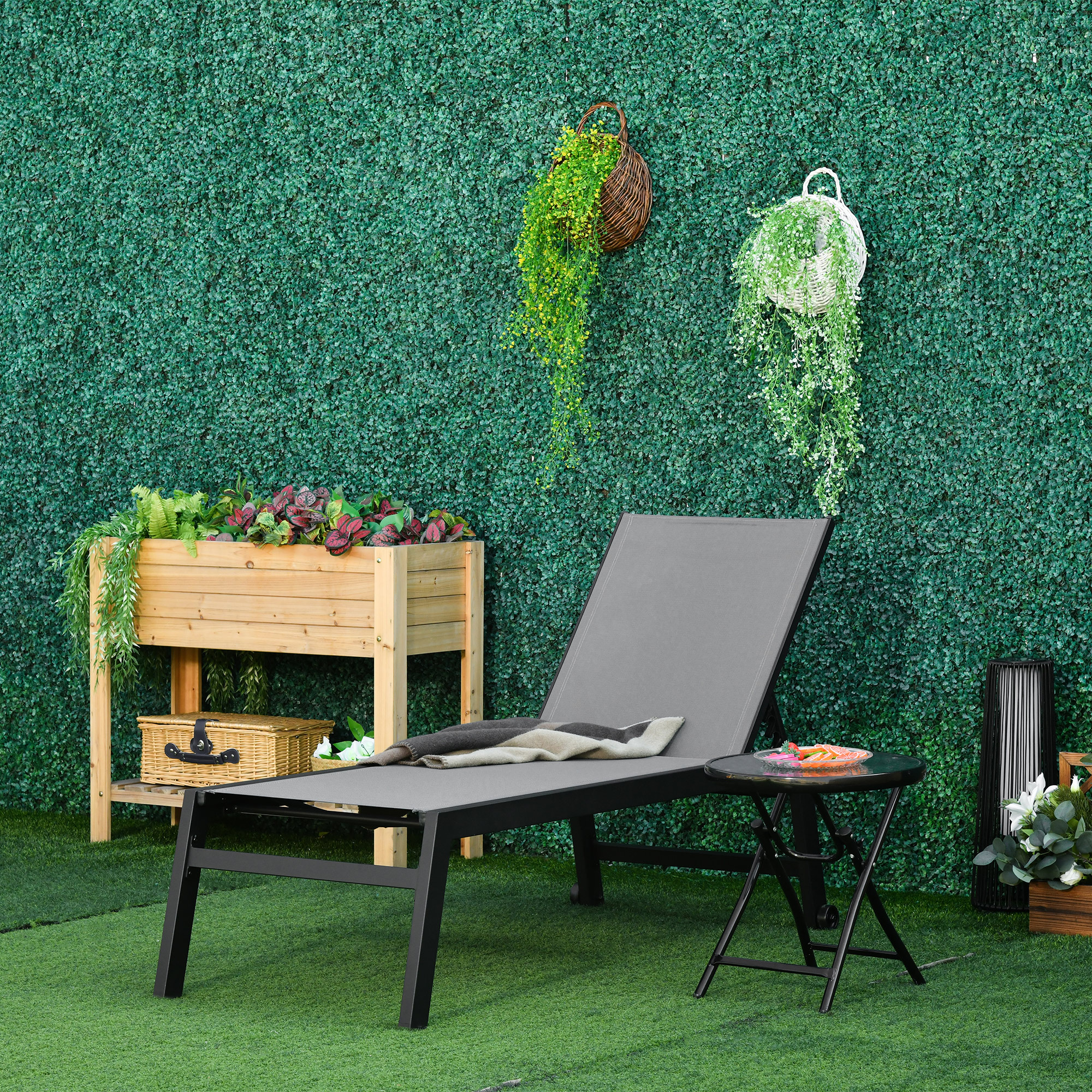 Sdraio grigio con coperta su erba sintetica di fronte a muro verde.
