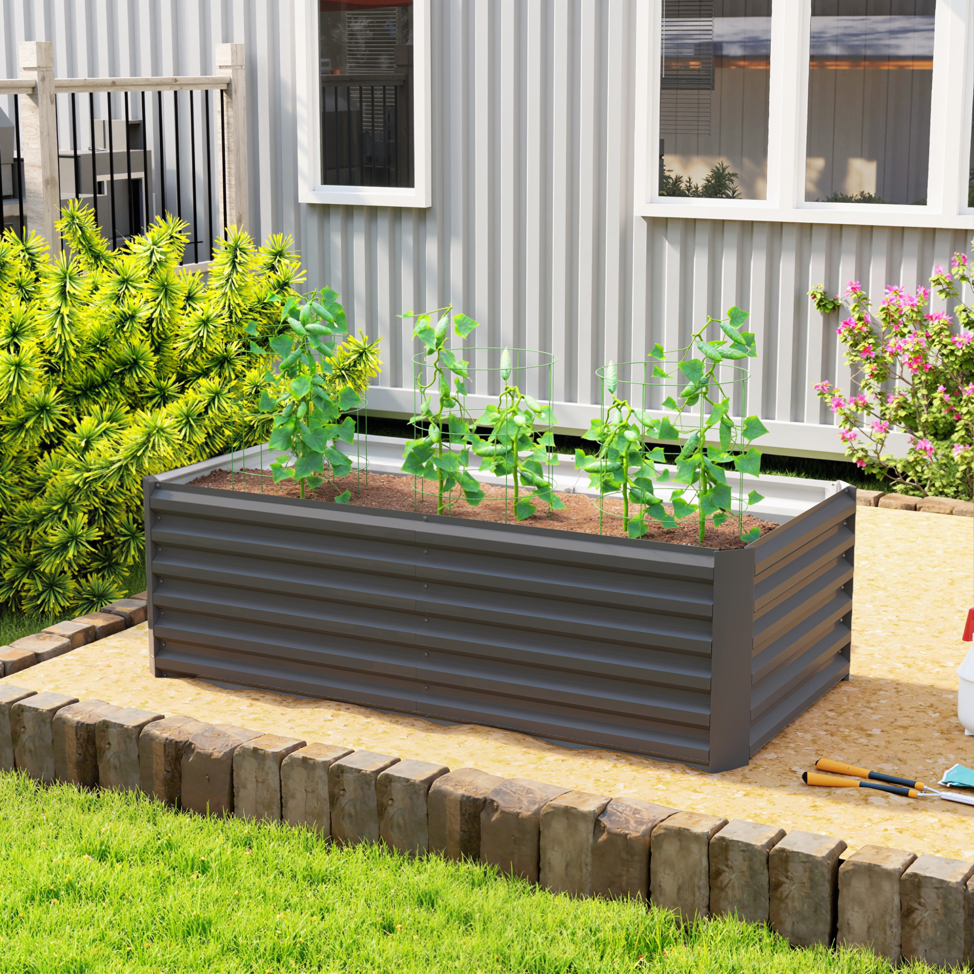 Un bancal elevado rectangular gris oscuro con plantas, en un entorno de jardín.