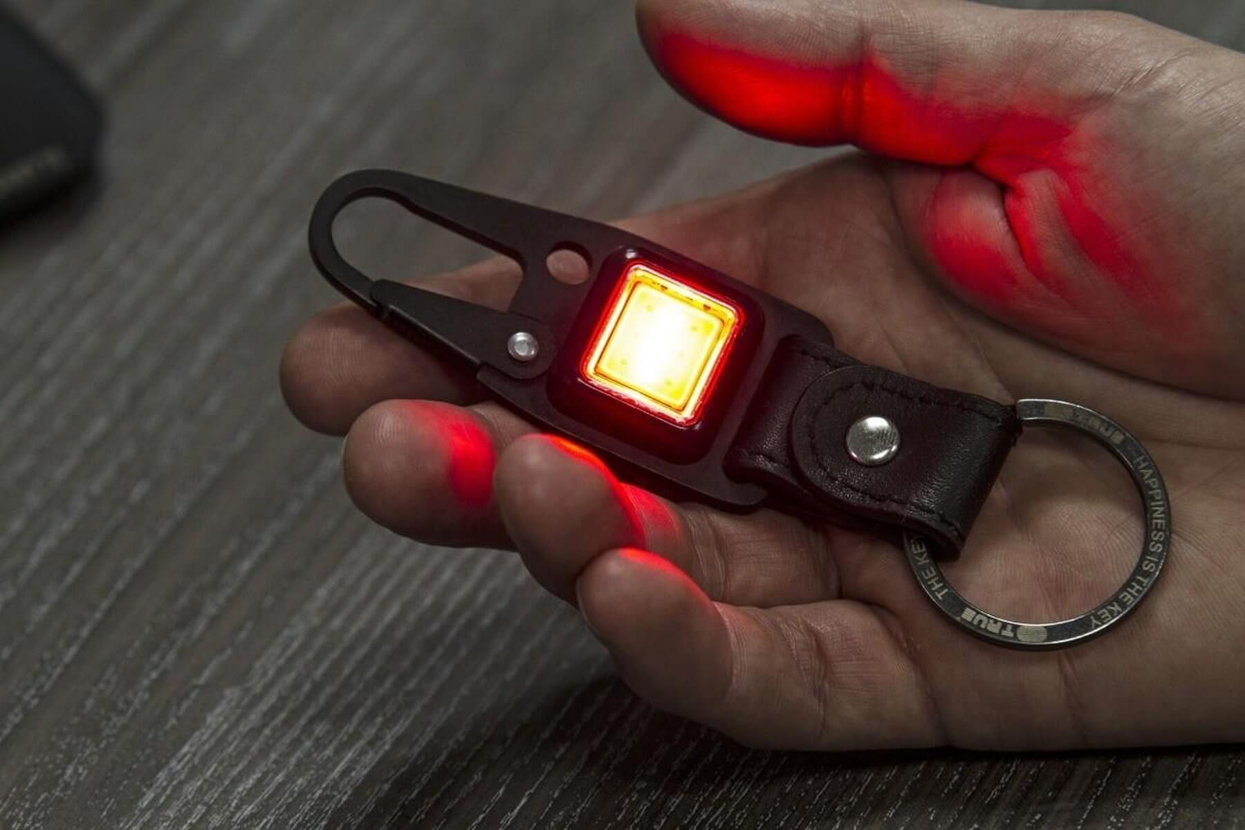 Una mano tiene un portachiavi nero con luce gialla brillante e bagliore rosso.