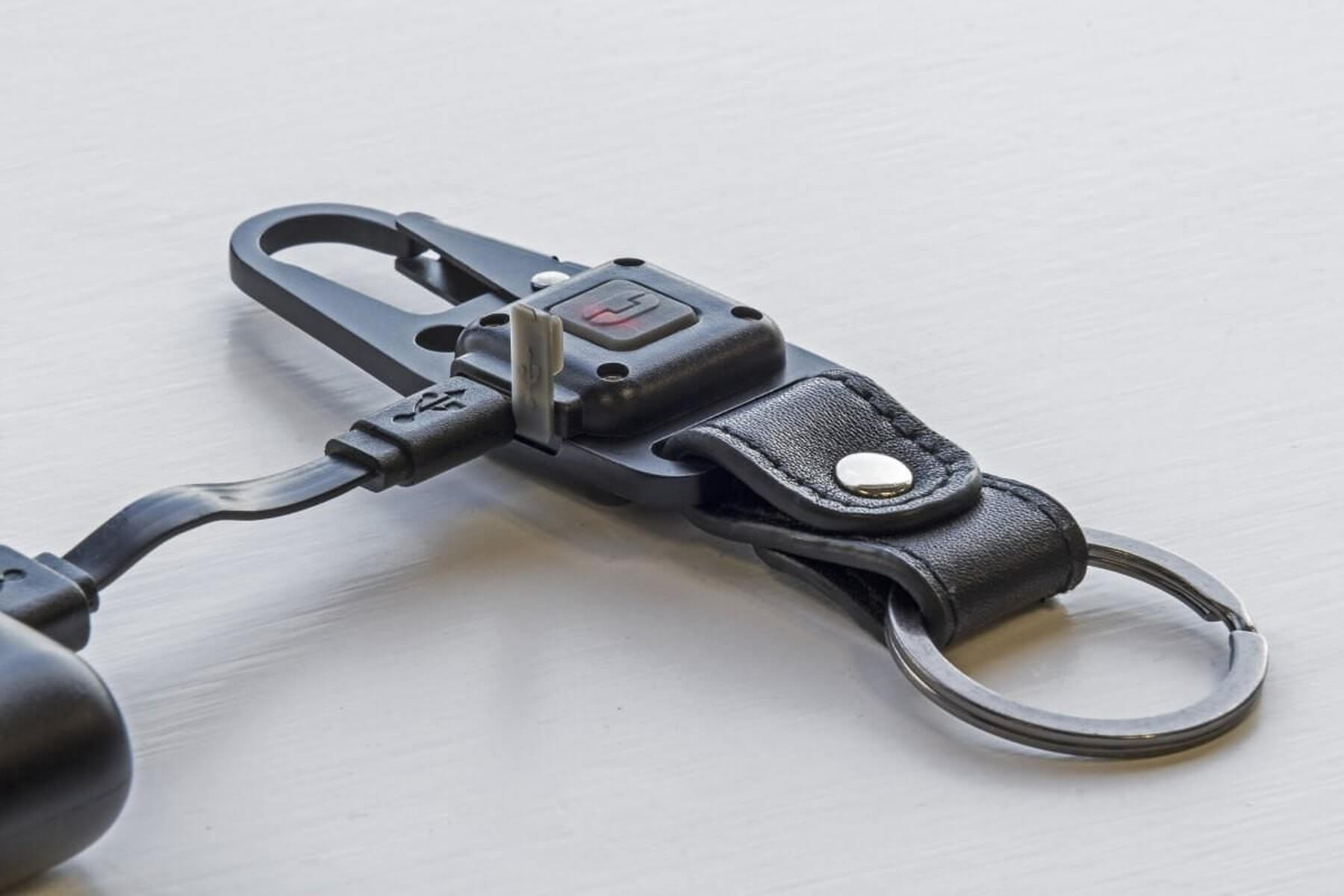 Portachiavi nero con cavo USB collegato, cinturino in pelle e anello metallico.