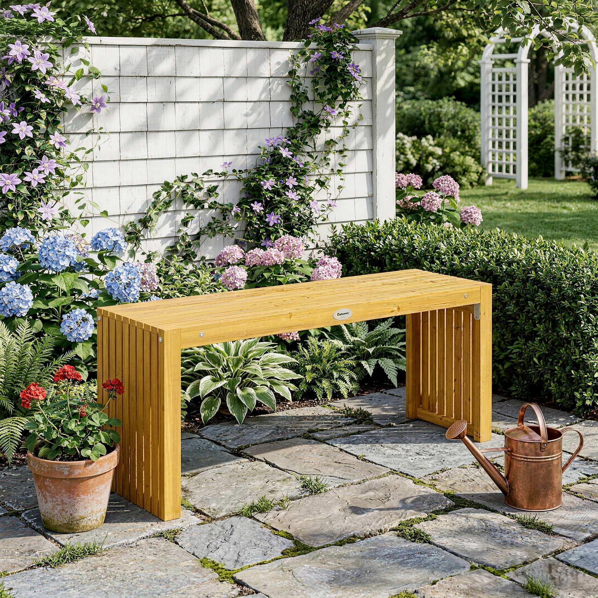 Banco de madera en jardín con hortensias, clemátides y regadera.