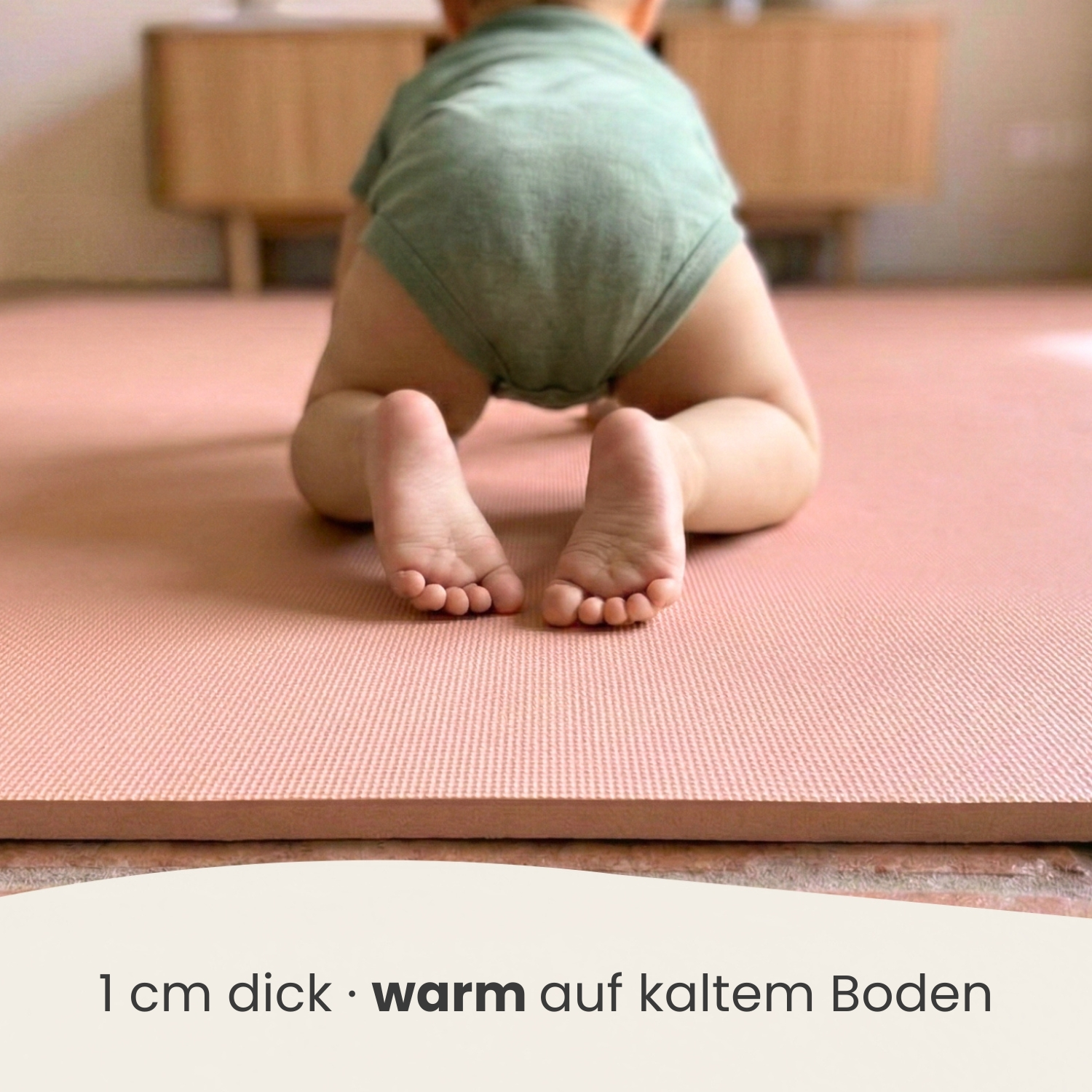 Baby krabbelt auf einer rosa Matte. Man sieht seine Füße und Beine.