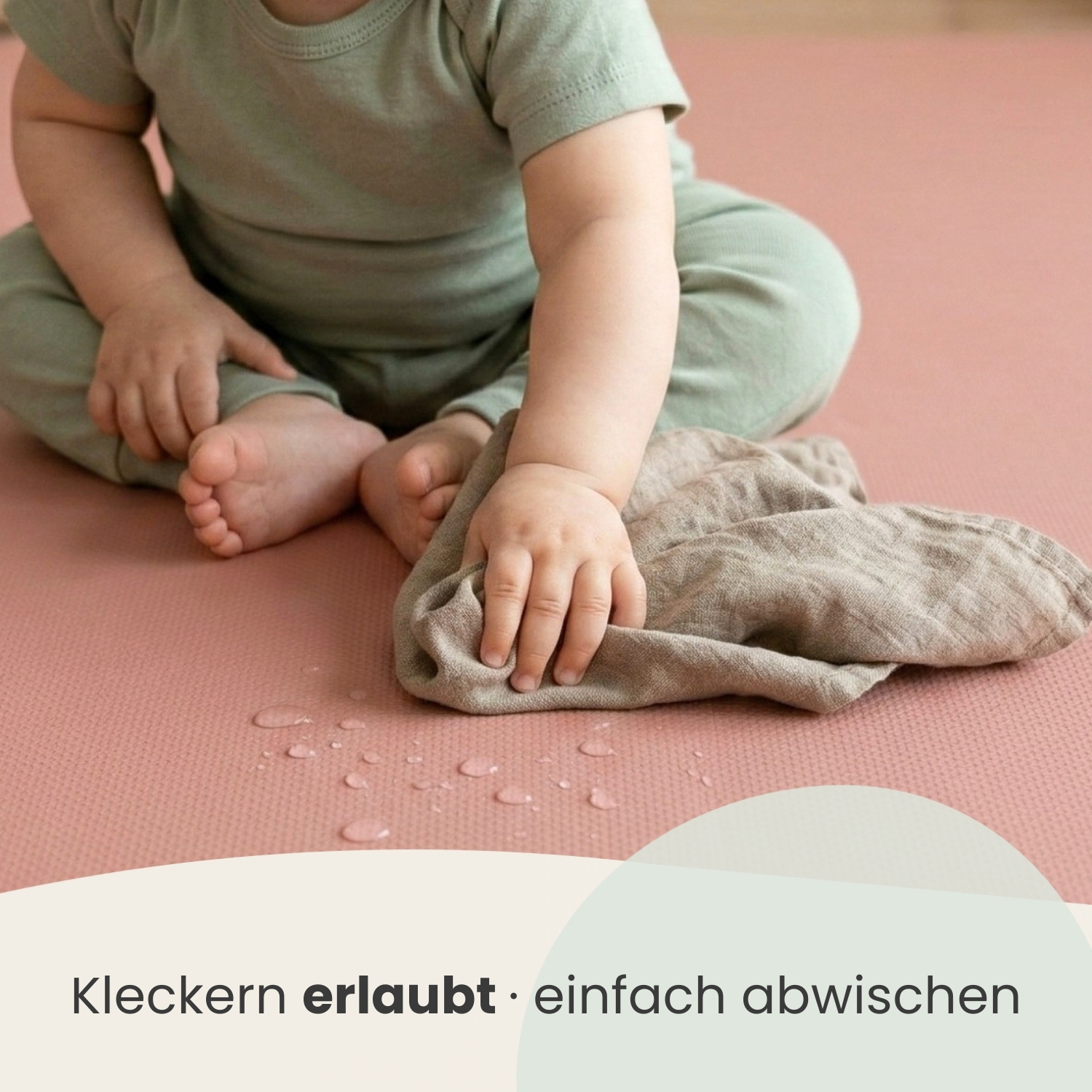 Ein Baby in einem grünen Outfit sitzt auf einer rosa Matte mit Wassertropfen.