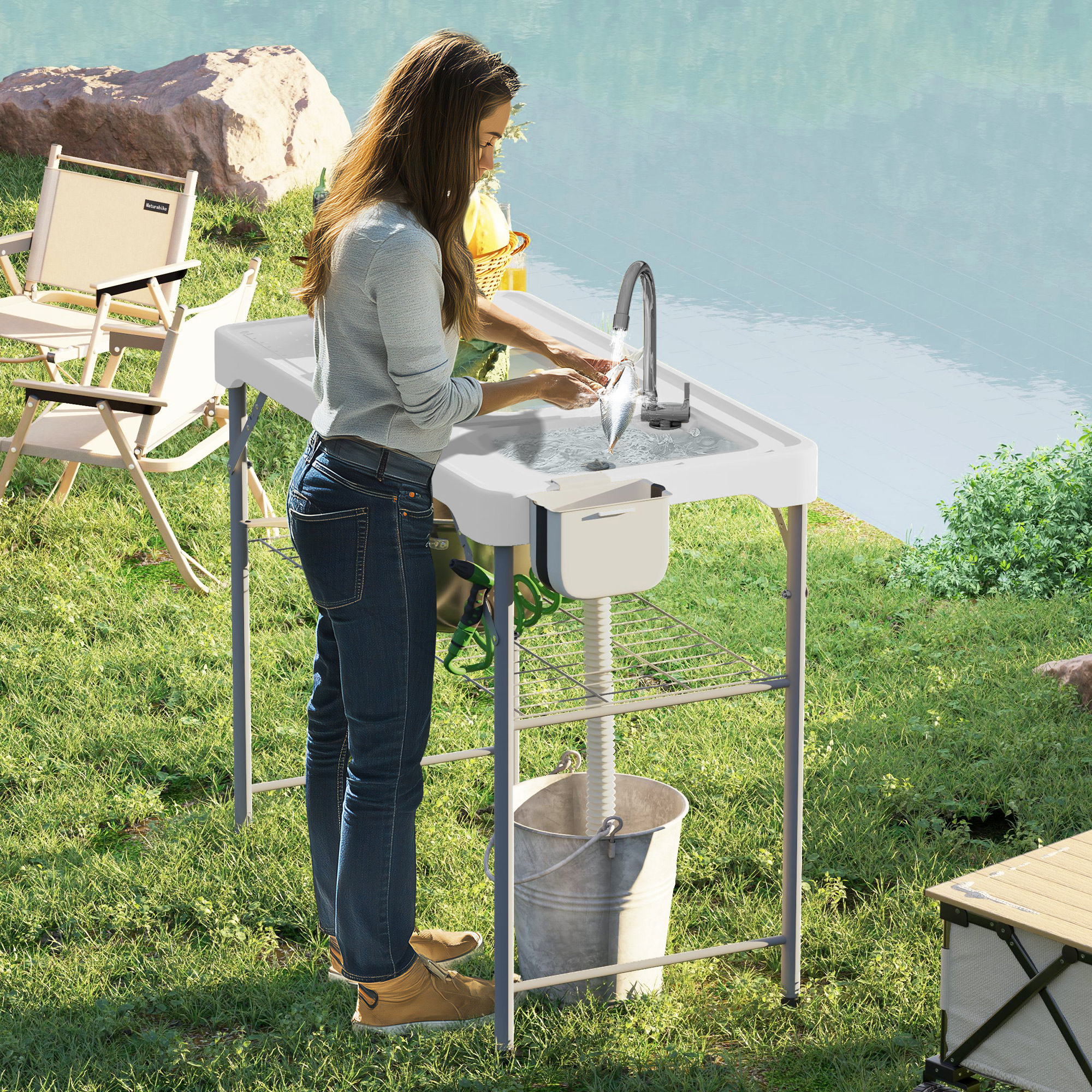 Mujer lavando pescado en un lavabo portátil junto a un lago, con sillas y mesa cerca.