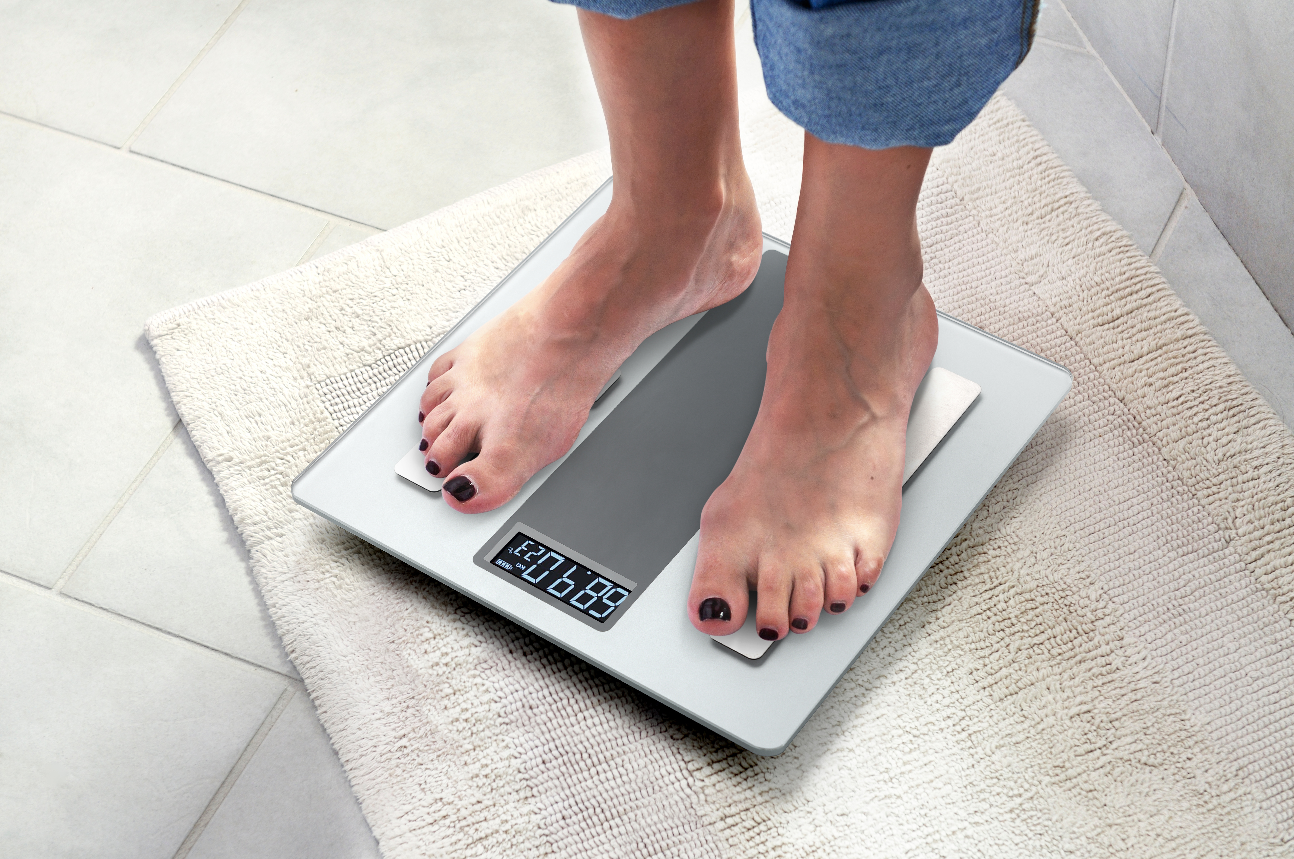 Feet on a digital scale showing 68.7 kg, placed on a rug.