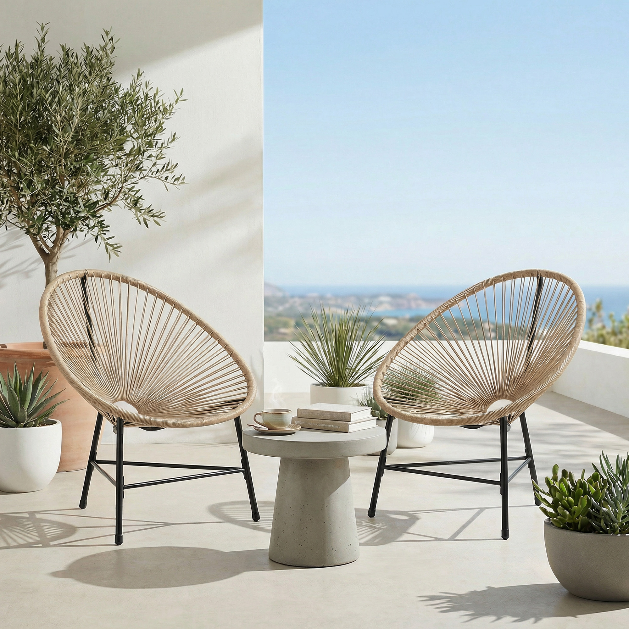 Due sedie intrecciate su un patio con vista sul mare. Un tavolino si trova tra loro.