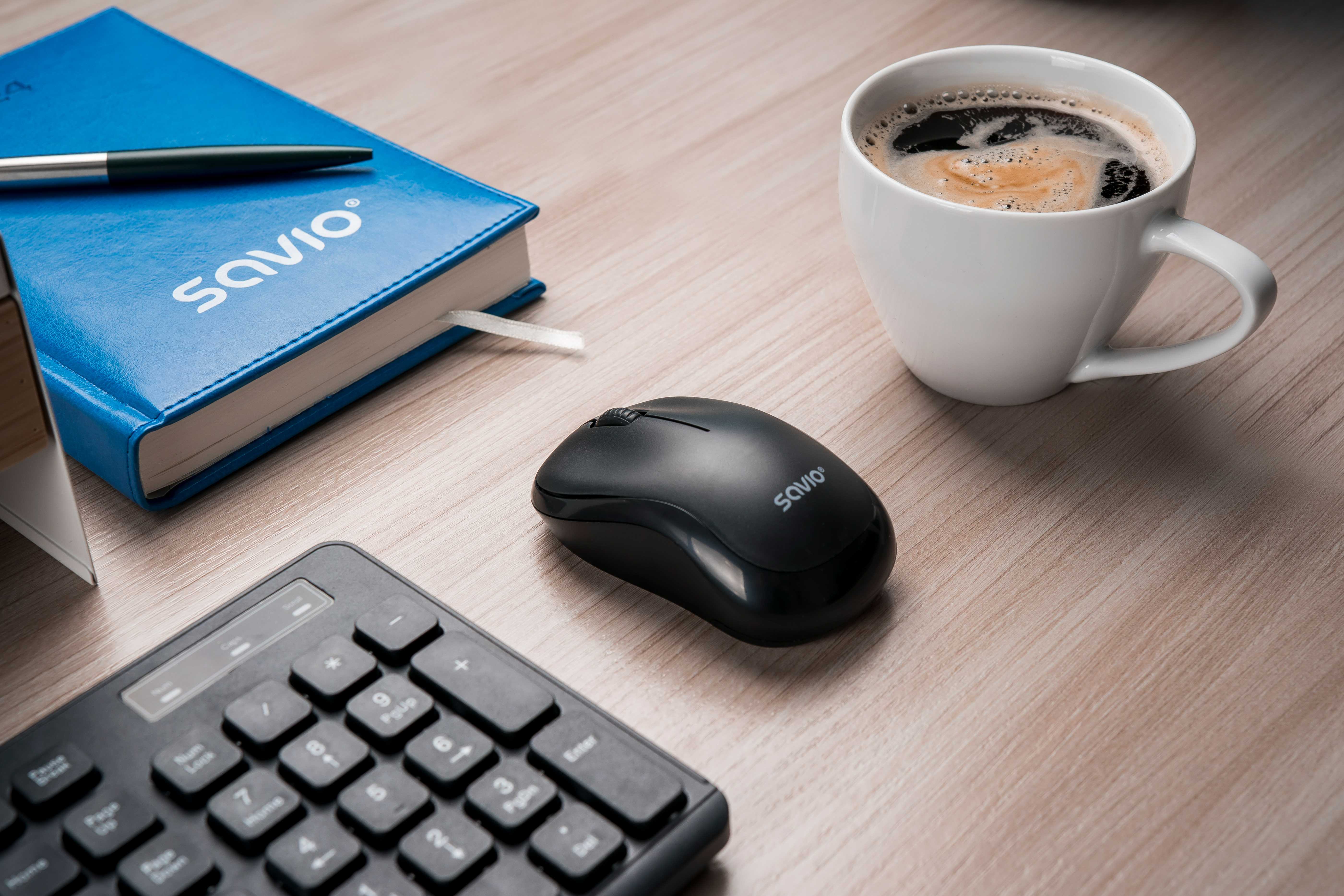 Czarna mysz, klawiatura, notatnik i filiżanka kawy na drewnianym biurku.