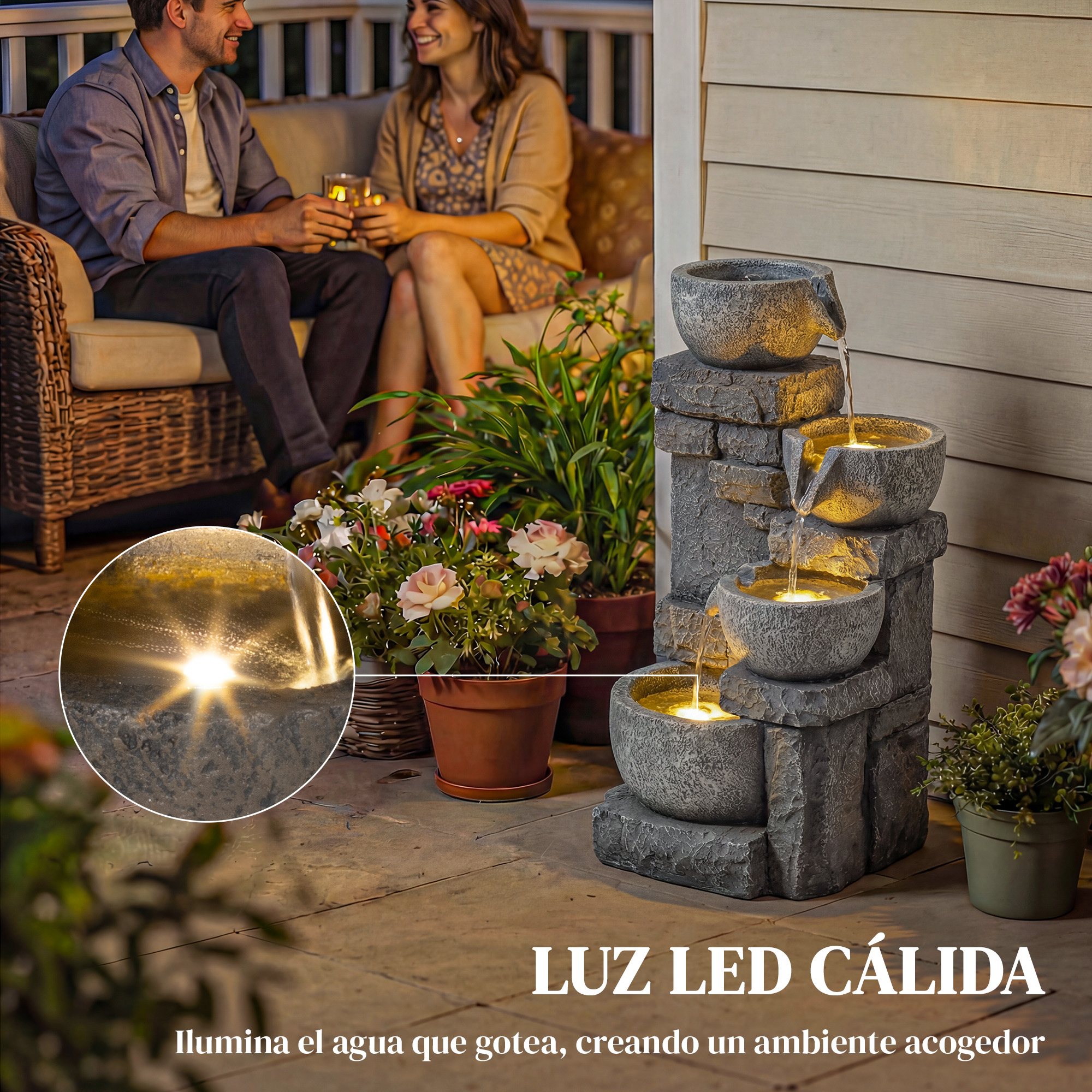 Una pareja bebe en un patio junto a una fuente iluminada y plantas.