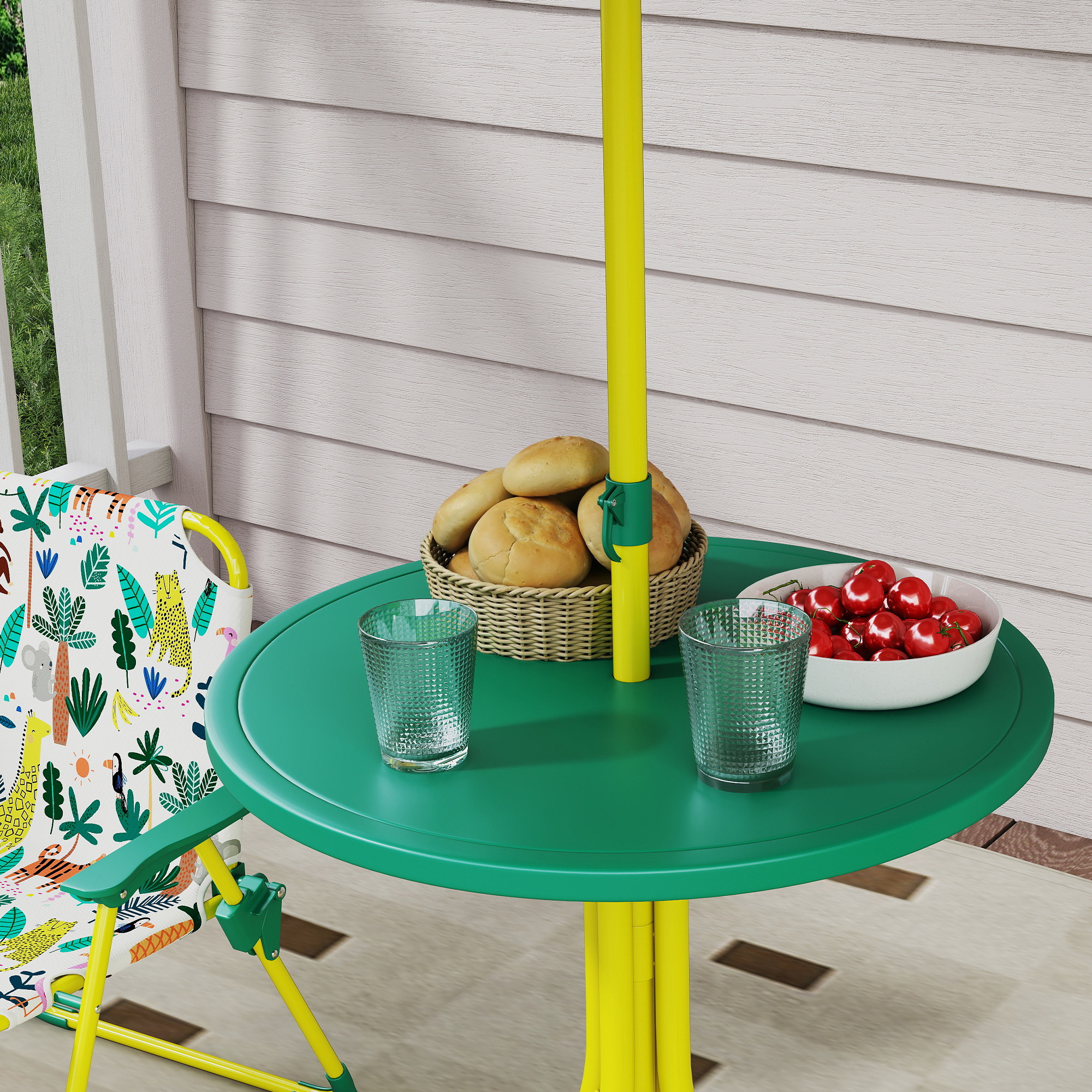 Tavolo verde con ombrellone giallo, panini, pomodori e bicchieri.