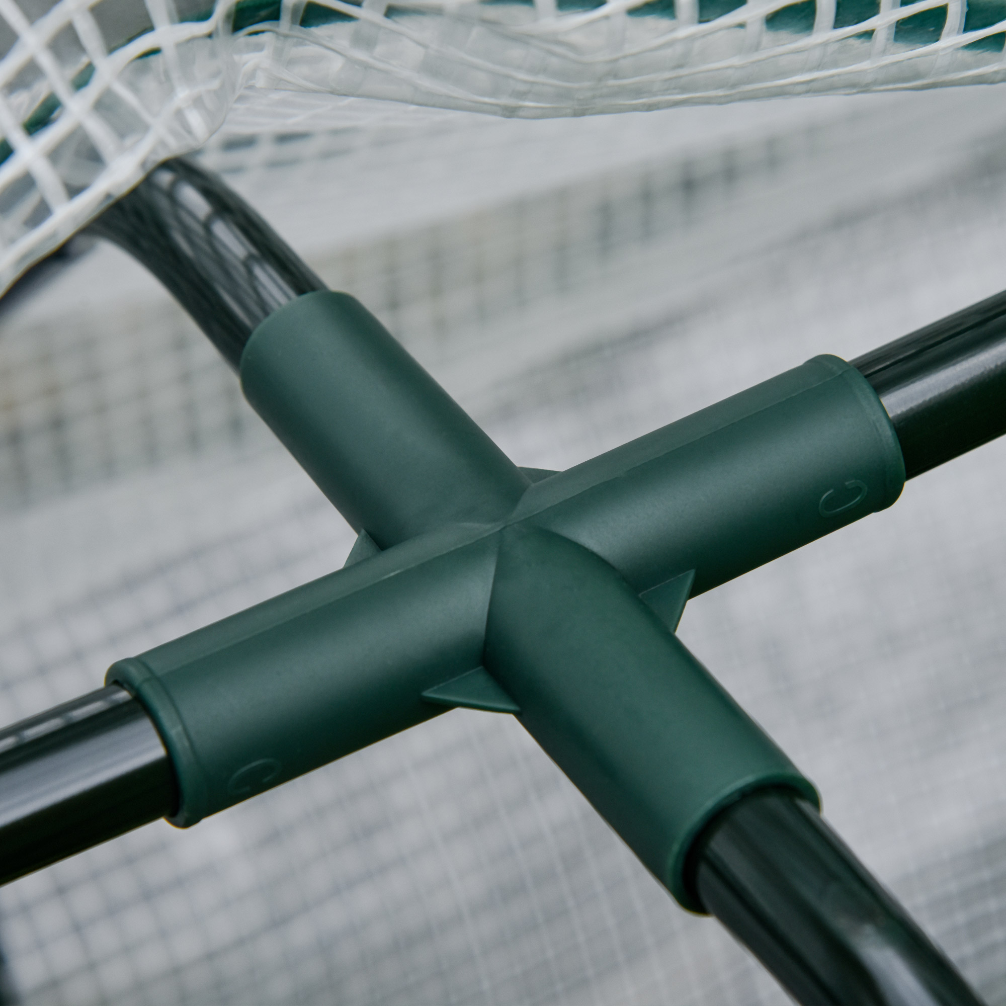Conector verde une tubos negros de invernadero con red blanca.