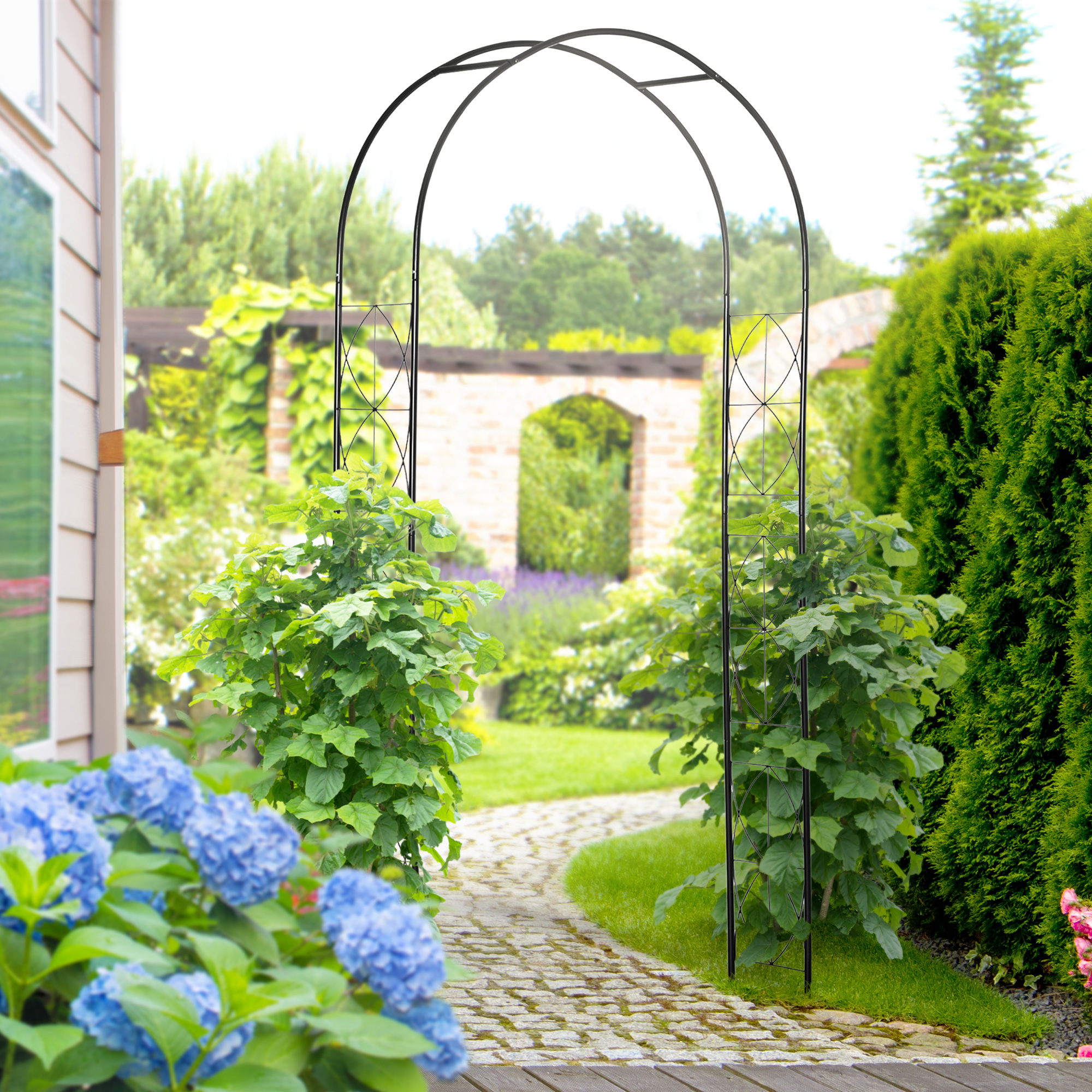 Un arco de metal negro en un jardín con flores y setos cuidados.
