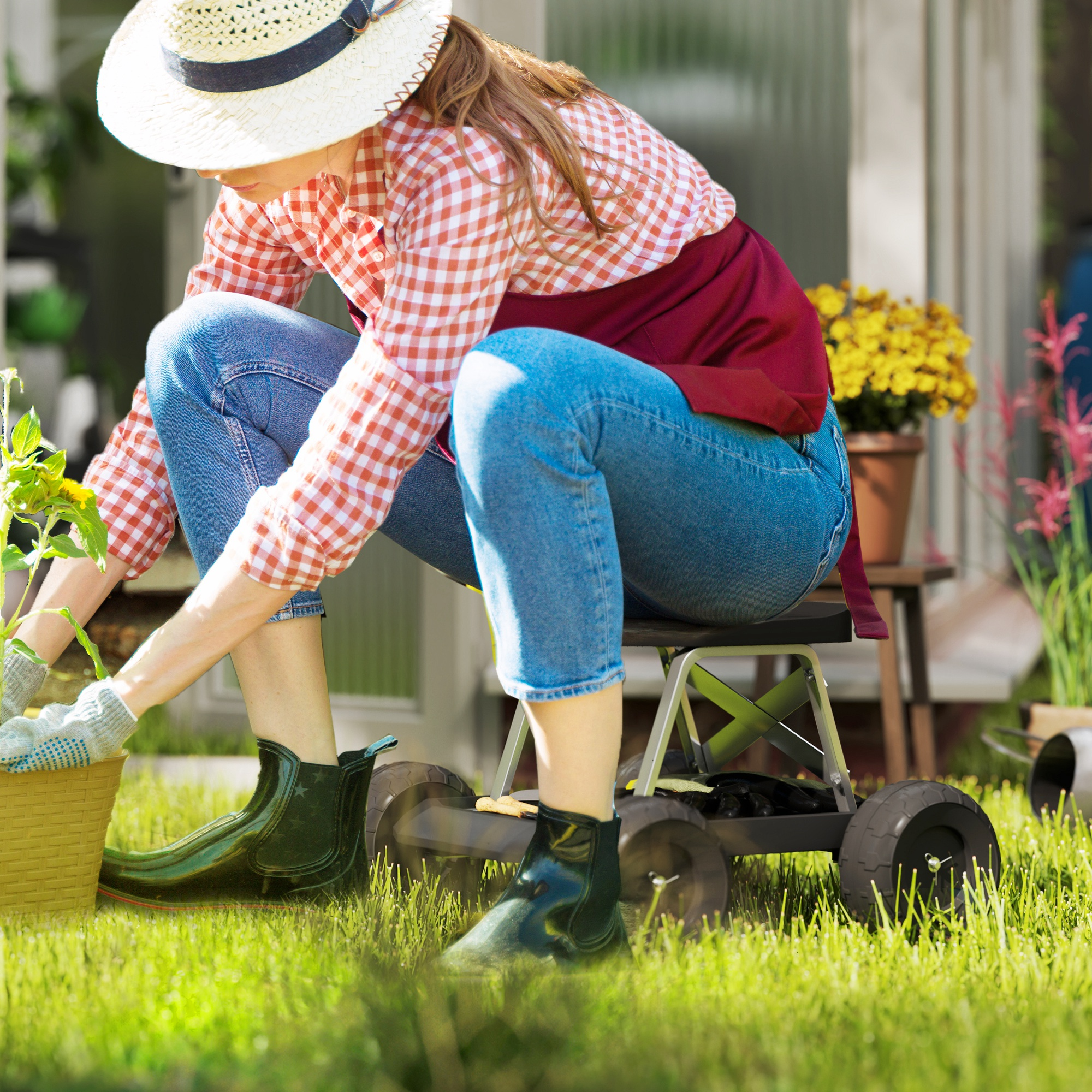 Una mujer con camisa de cuadros y jeans planta una plántula en el jardín en un taburete rodante.