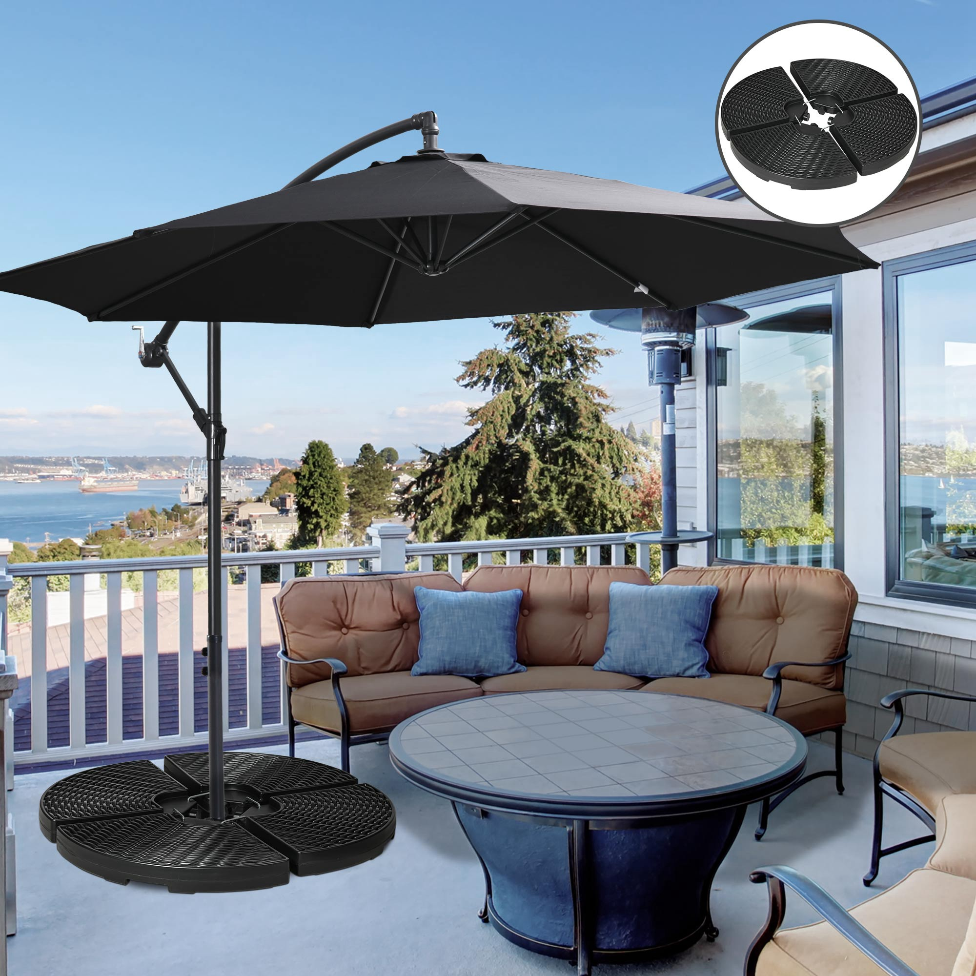 Un parasol de patio negro con base cruzada se alza en un balcón con muebles y vista al mar.