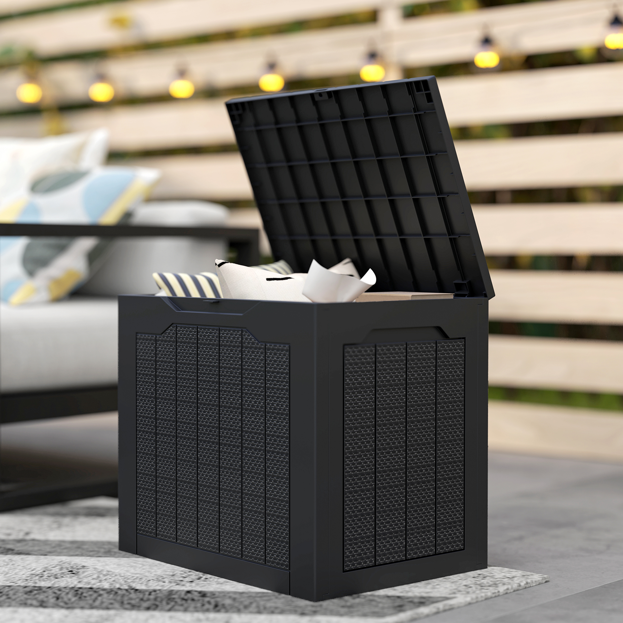 Caja de almacenamiento negra con tapa abierta, llena de cojines y papel en un patio exterior.