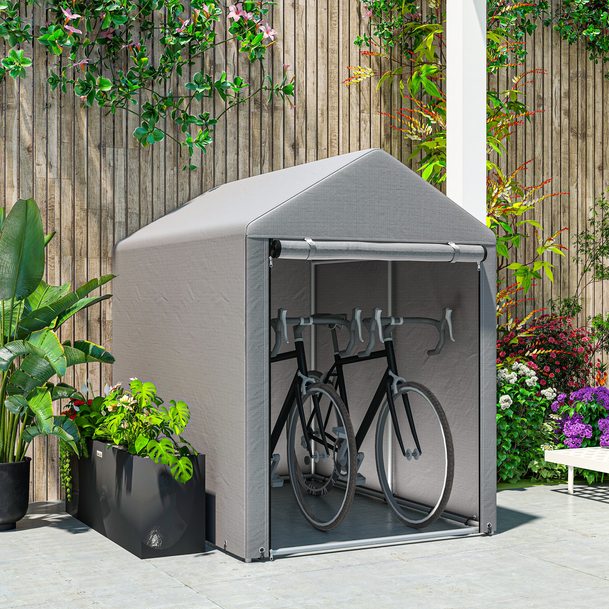  cobertizo gris para bicicletas con dos bicicletas dentro, en un patio pavimentado con plantas.