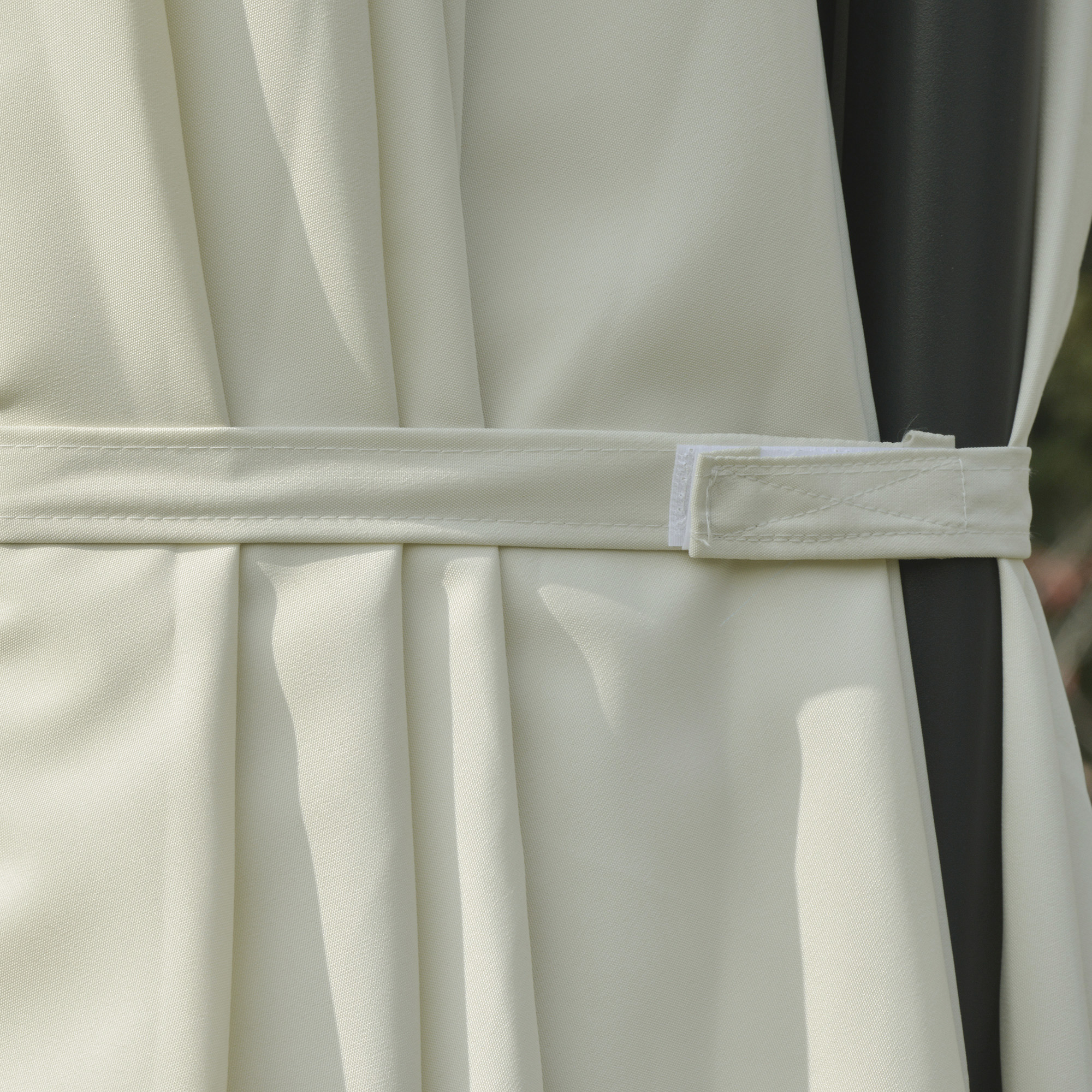 Tela beige con pliegues y una correa de velcro blanca enrollada en un poste oscuro.