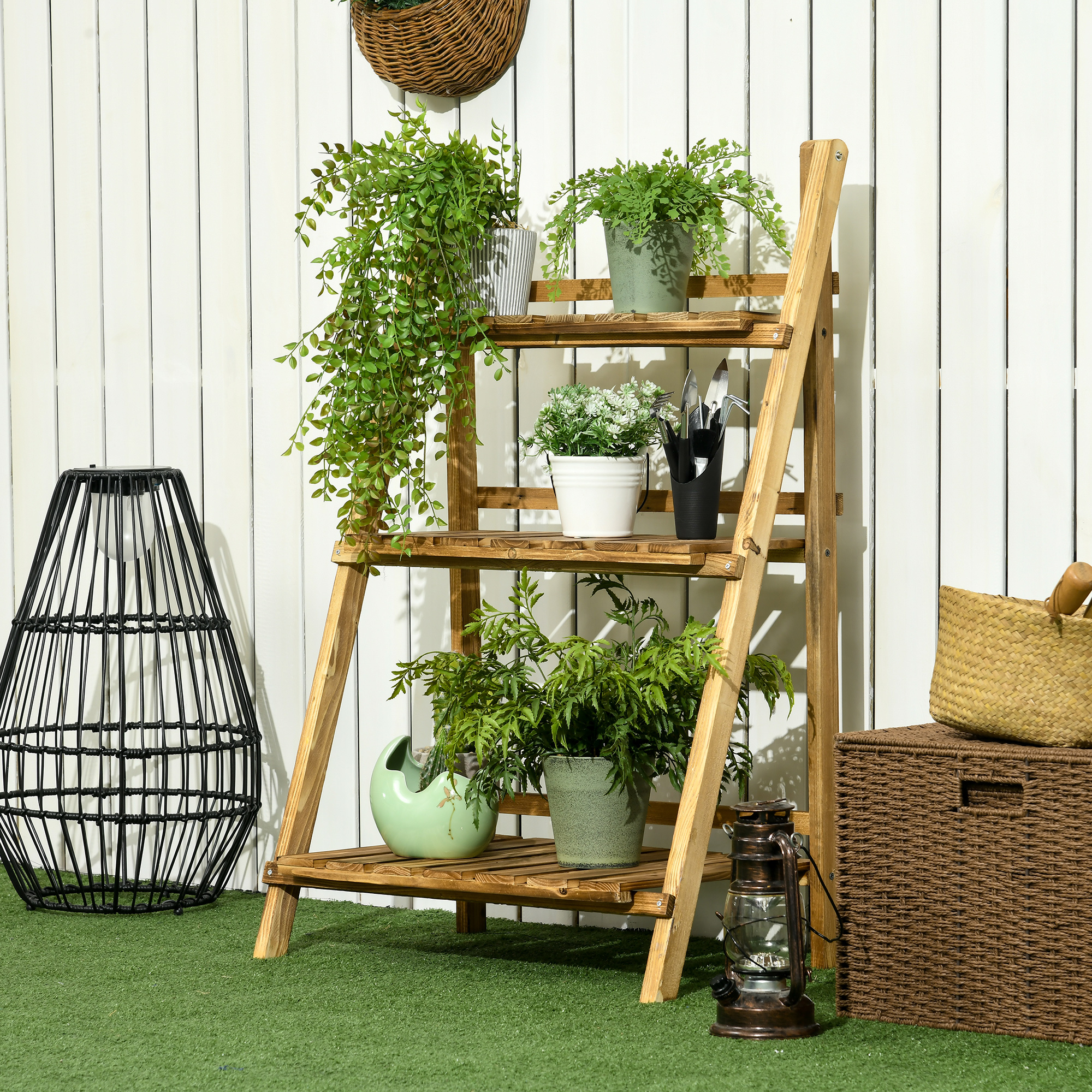 Estante de madera con plantas, linterna, cesta y caja sobre césped artificial.